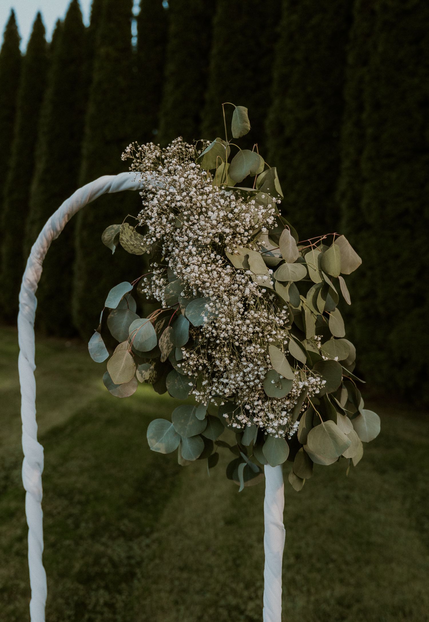 Delicate baby's breath and eucalyptus decorate white poles for an outdoor ceremony.