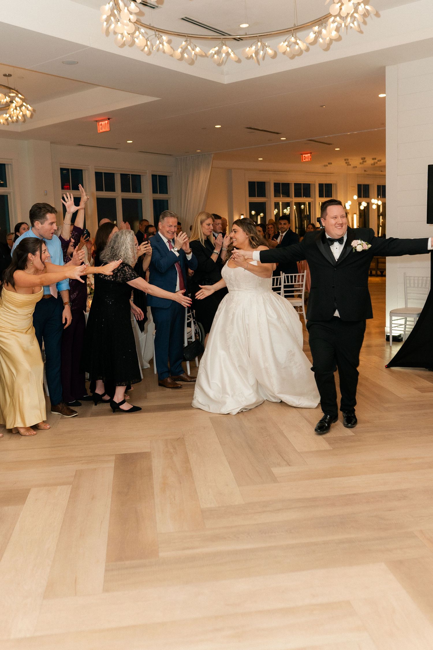 Bride in white gown and groom in tuxedo make grand entrance to cheering guests at wedding reception.