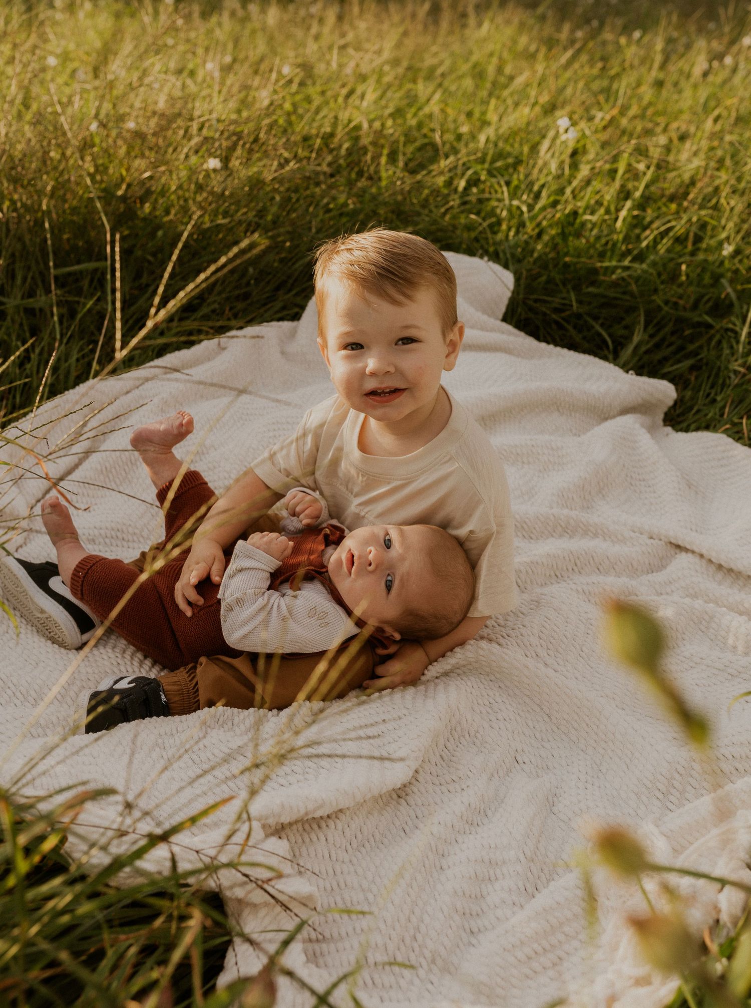 Young child lying on white blanket in grassy field during sunset.