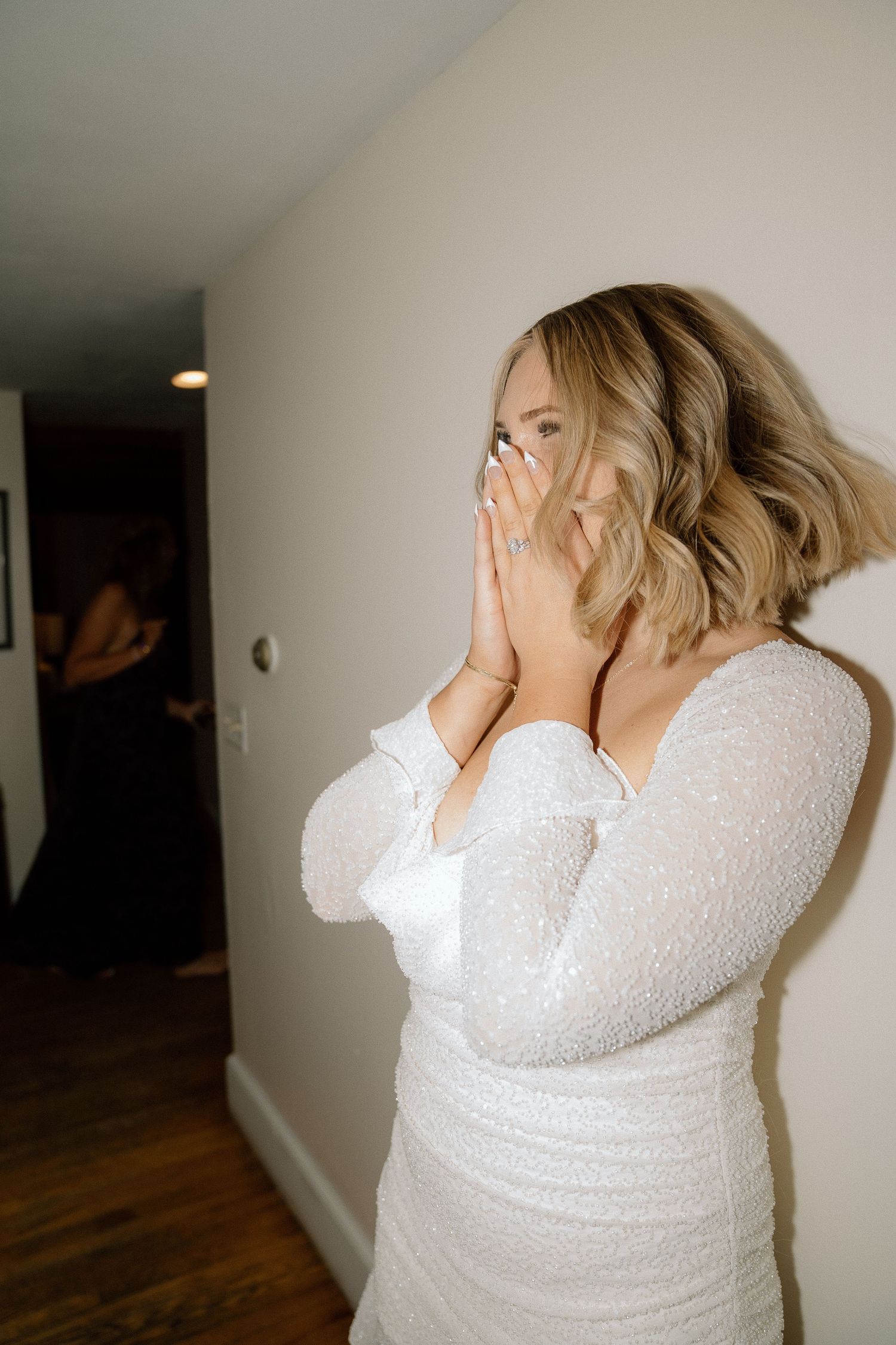 A person in a white lace dress covers their mouth in joyful surprise.