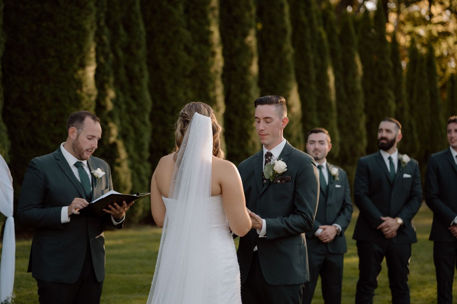 Wedding ceremony in progress with bridal party lined up against backdrop of cypress trees.