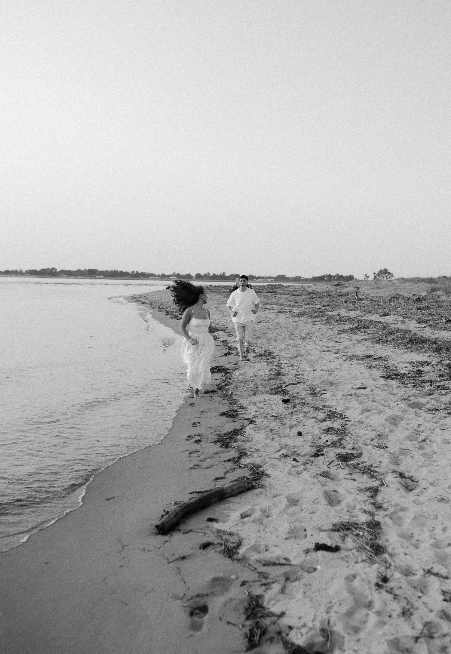 A couple running along a beach shoreline in black and white photography.