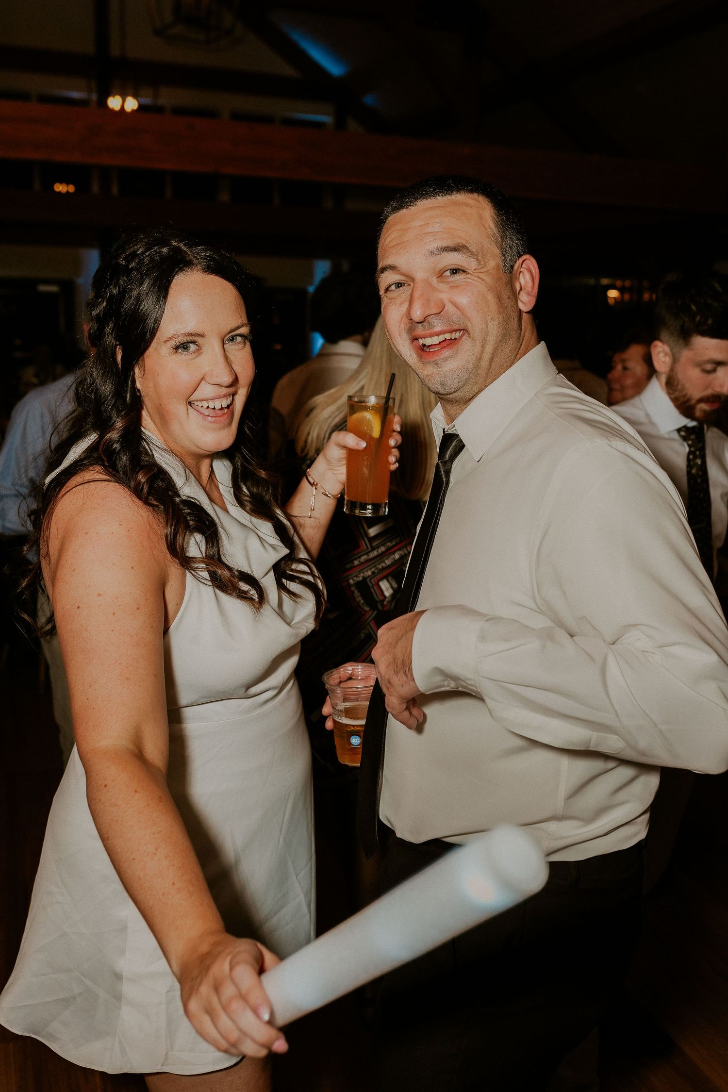 A couple dances together at a dimly lit wedding reception venue, with the person in white leading their dance partner.
