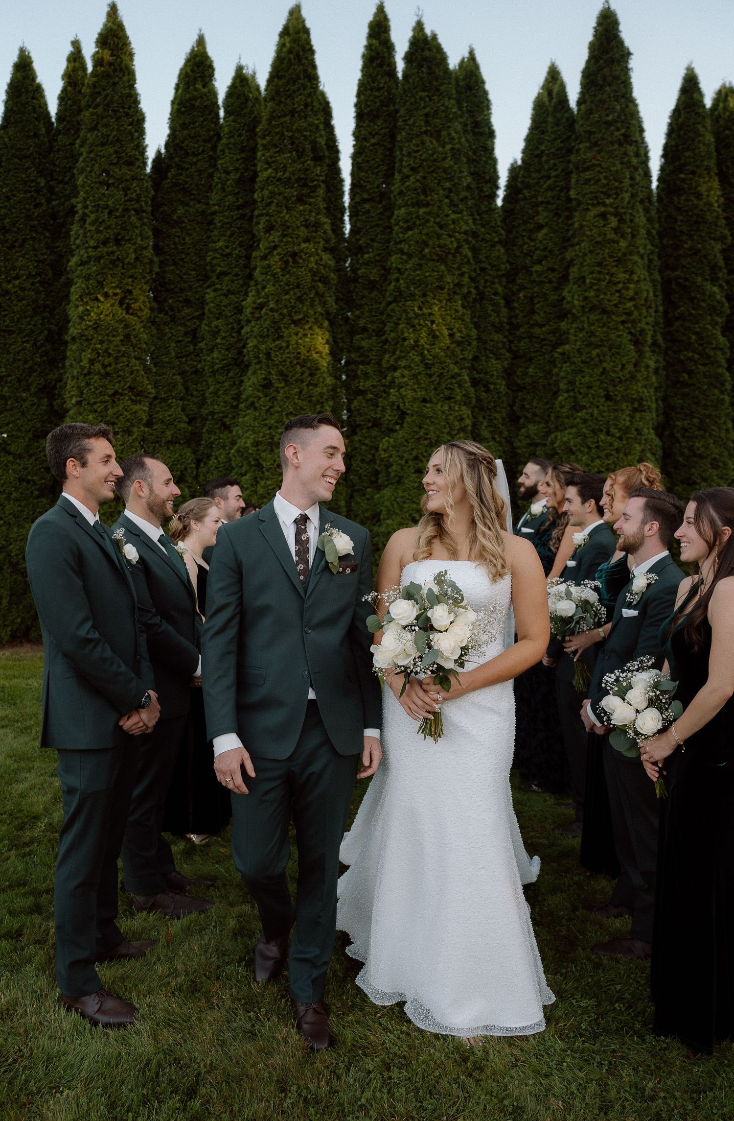 Candid moment between wedding party members against a backdrop of tall cypress trees.