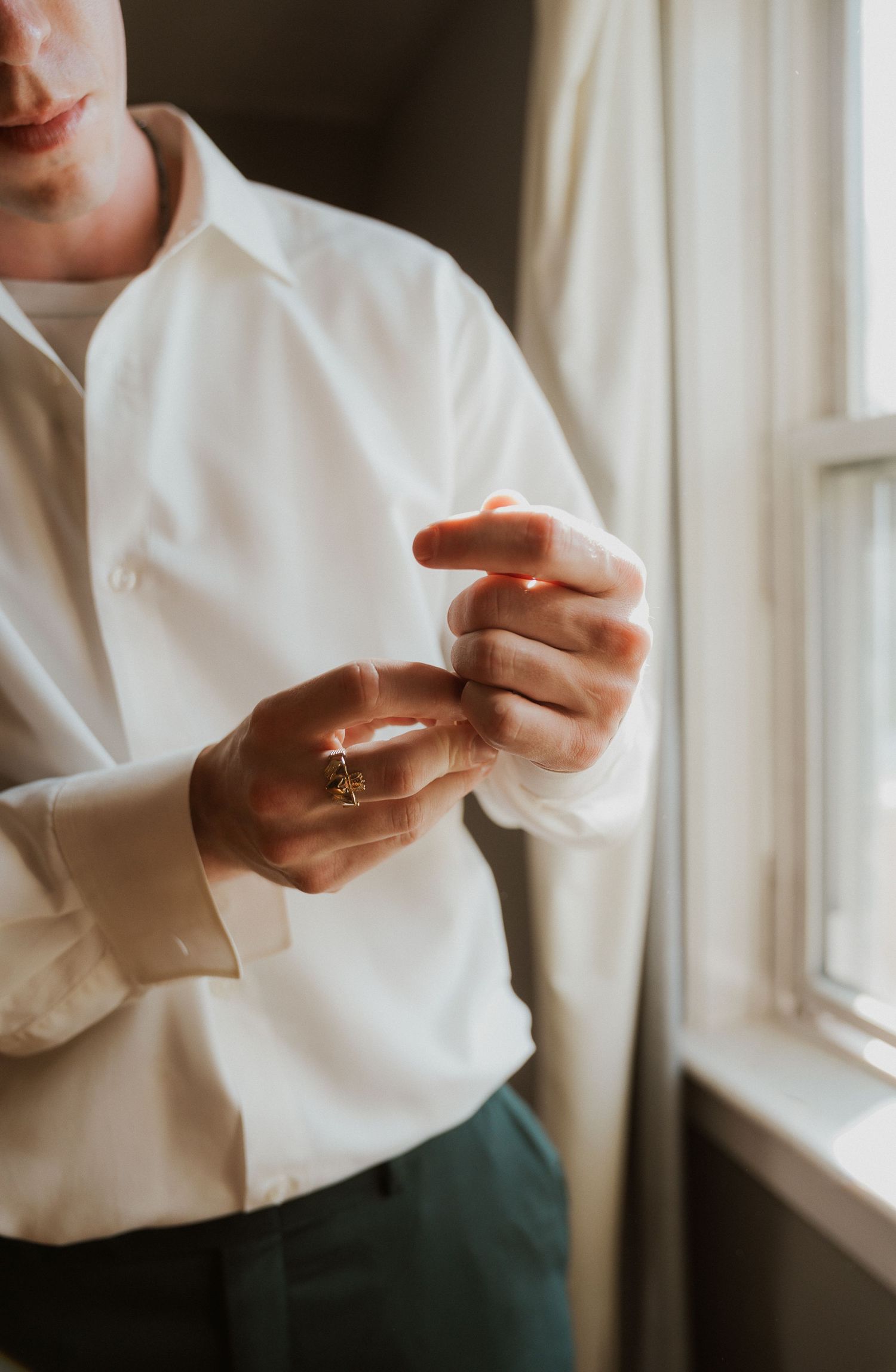 Hands delicately adjusting jewelry near a window in natural light.