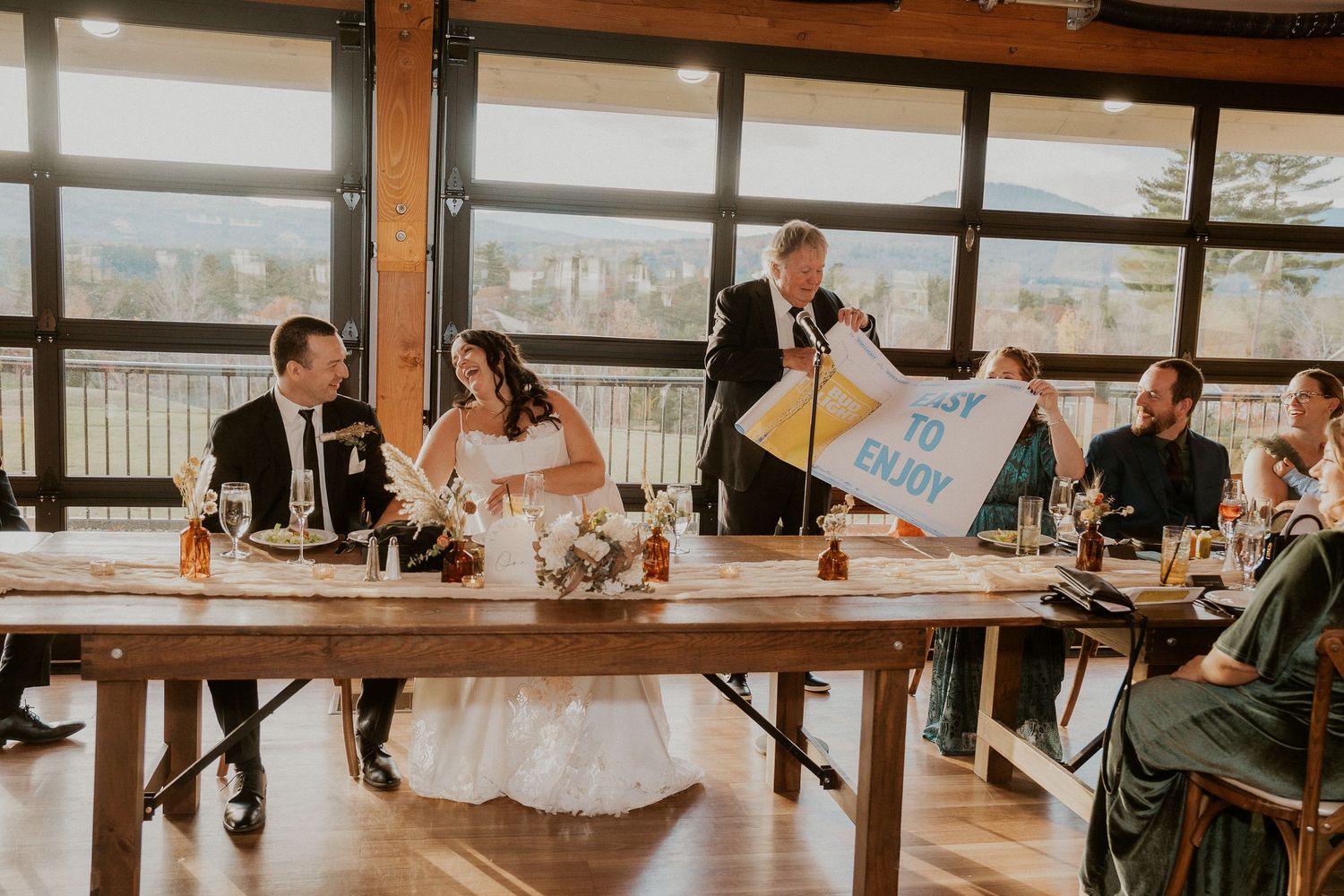 Long banquet tables set for wedding reception in rustic wooden venue with panoramic mountain views.