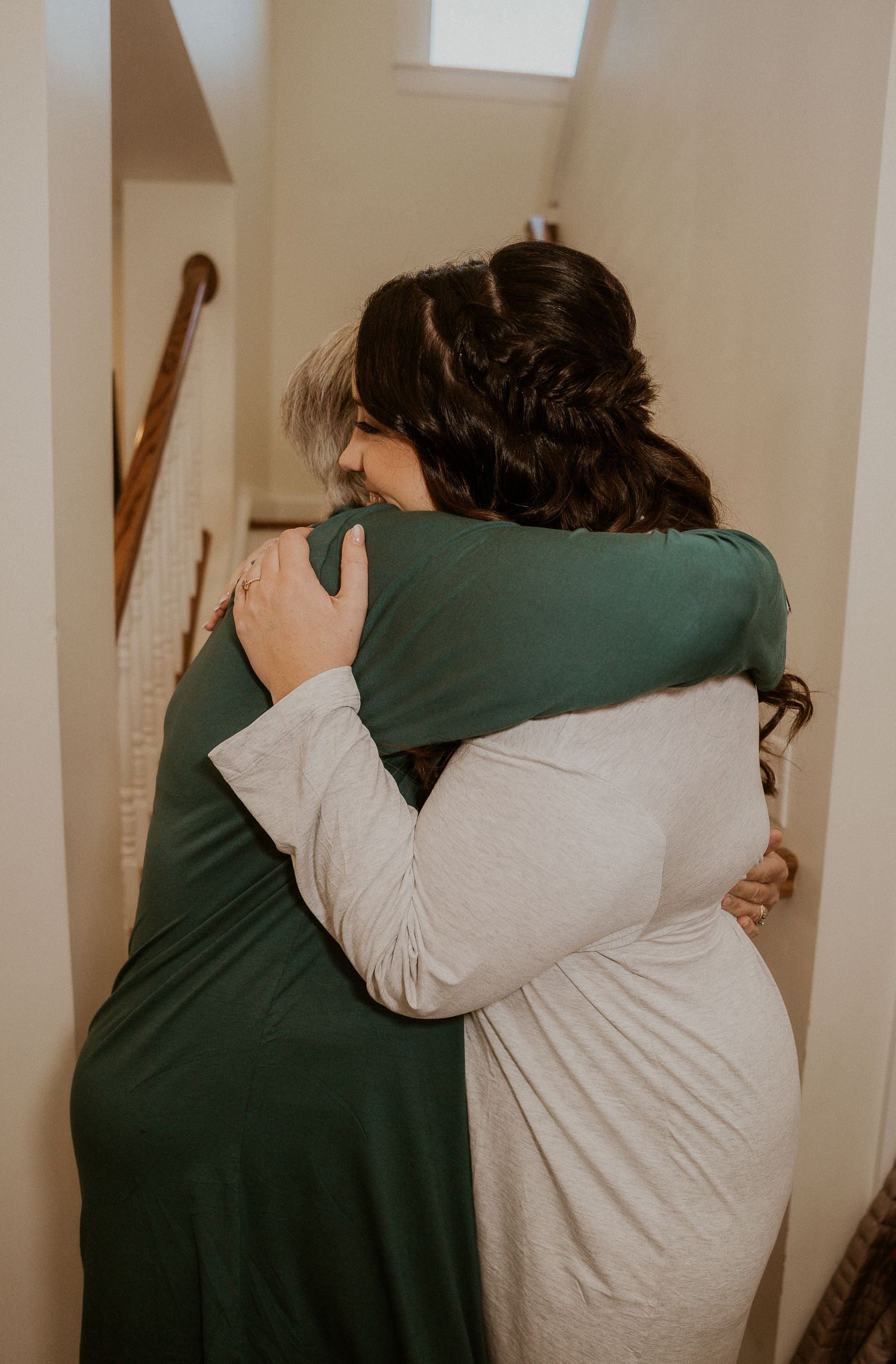 Two people share an emotional embrace in a hallway, one wearing green and one wearing beige.
