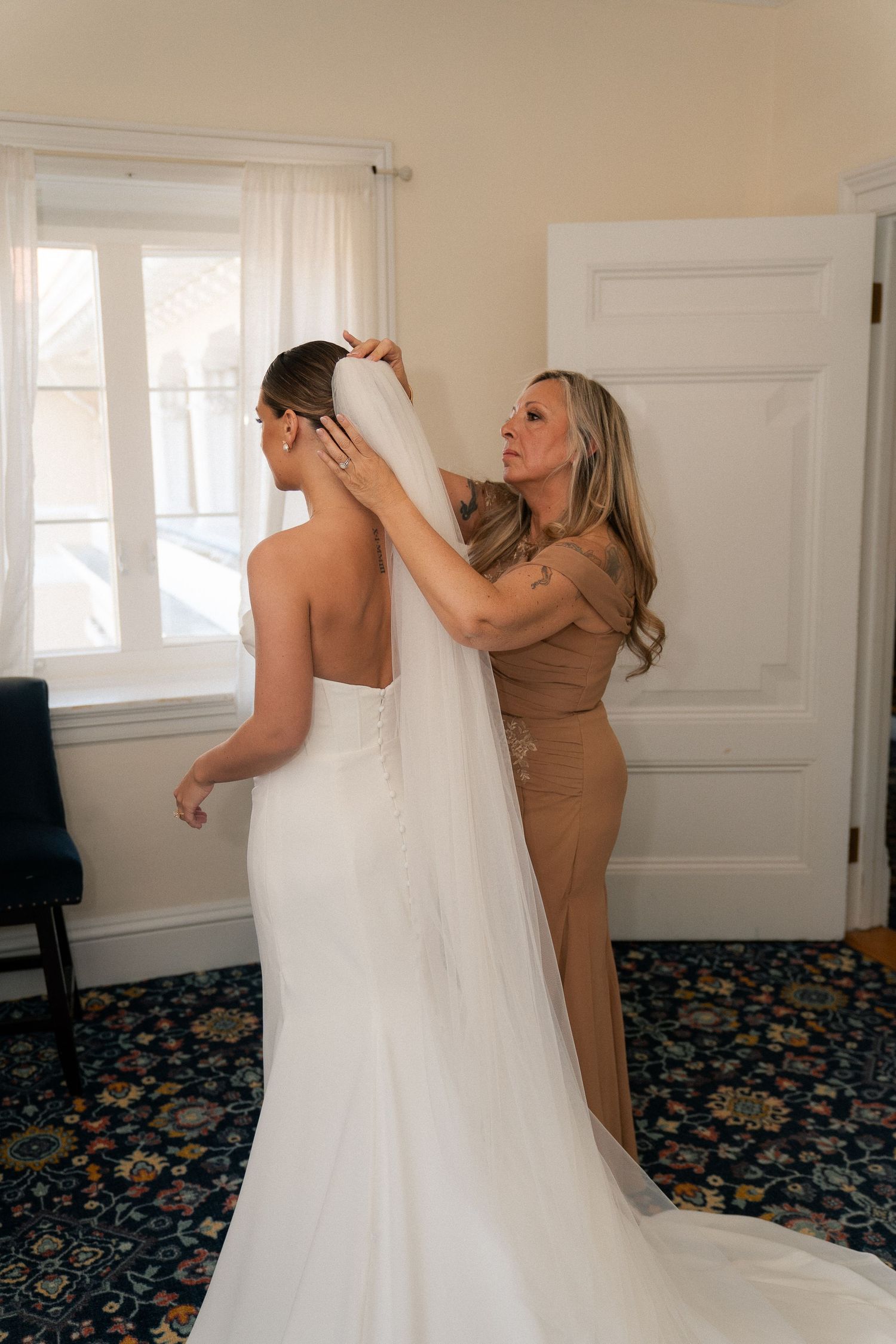 A woman helps a bride put on her veil in a elegant room before the wedding ceremony.
