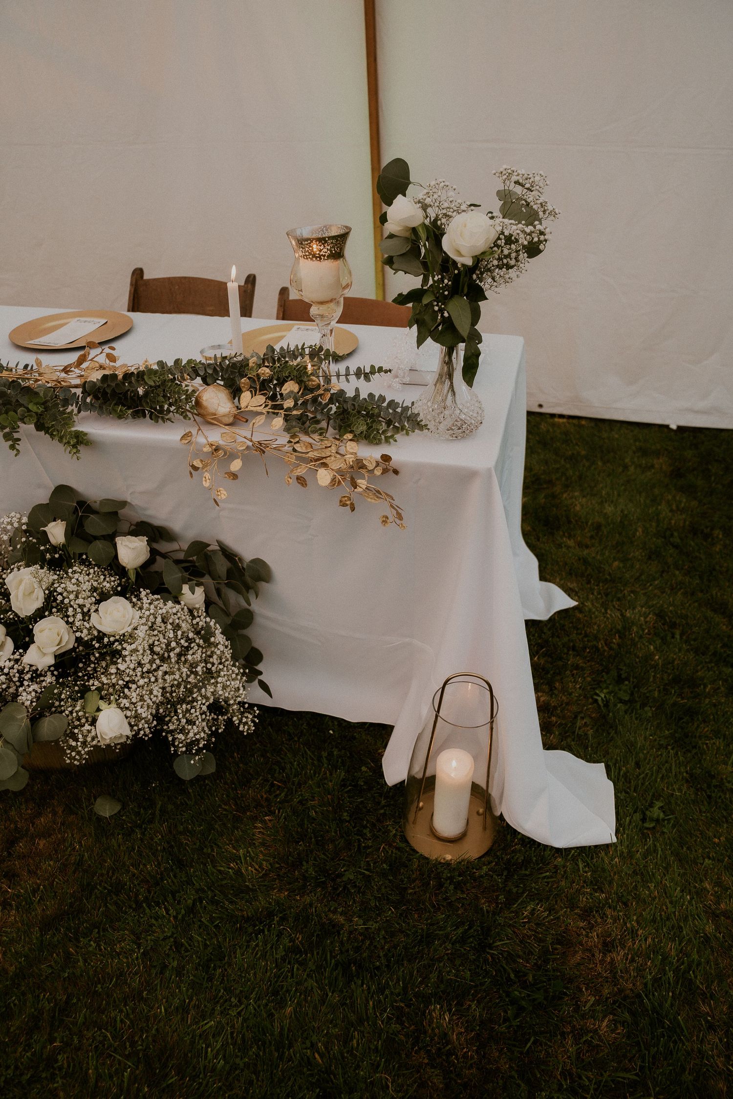 Wedding reception decor featuring white tablecloths and floral arrangements under tent lighting.