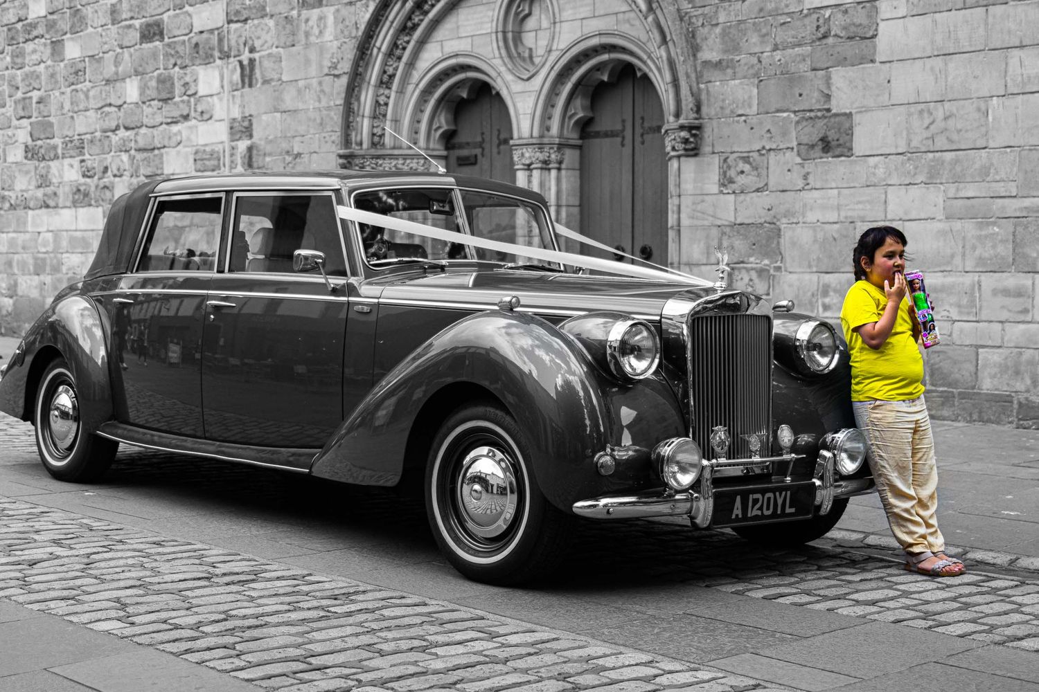 street photography of a child casually leaning against a wedding car in front of the church by Gerard Su Photography.