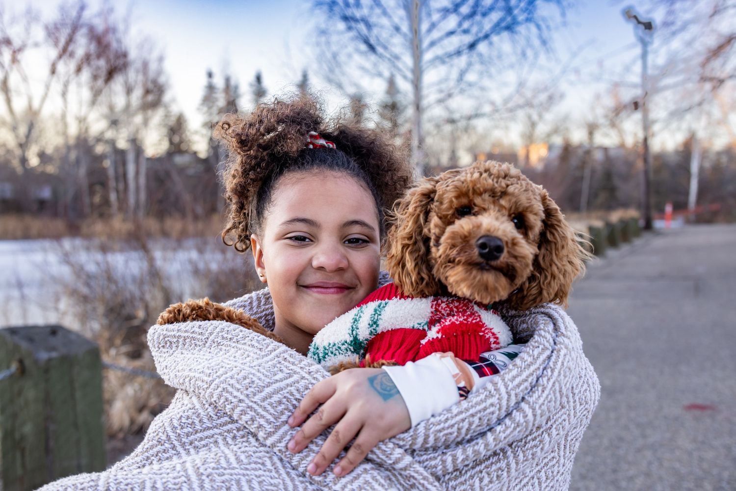 Young woman wrapped in blanket smiling while holding a fluffy golden doodle puppy outdoors in winter.
