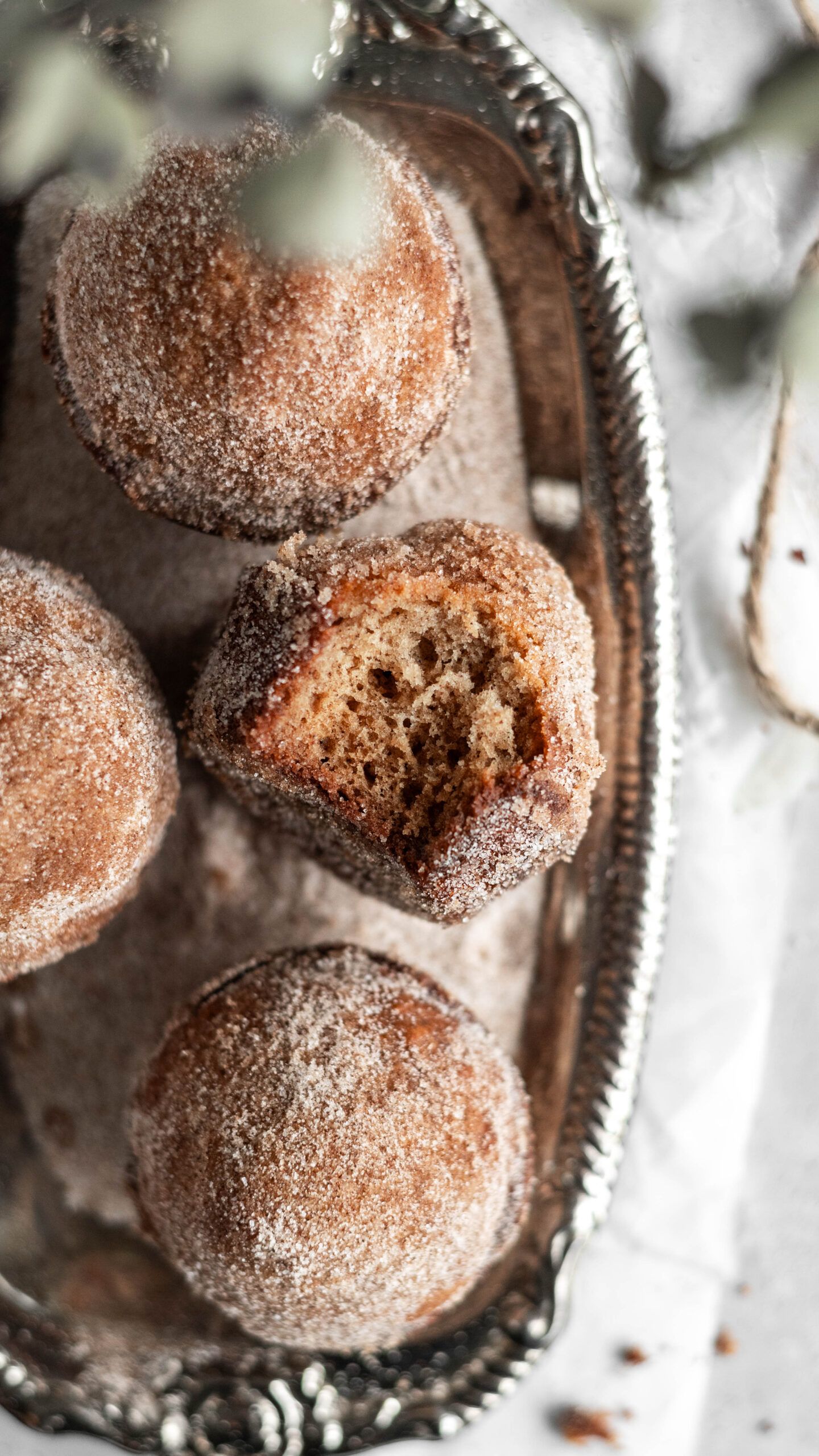 Freshly baked sugared donut holes shown in vintage silver tray with one broken open revealing soft interior texture.