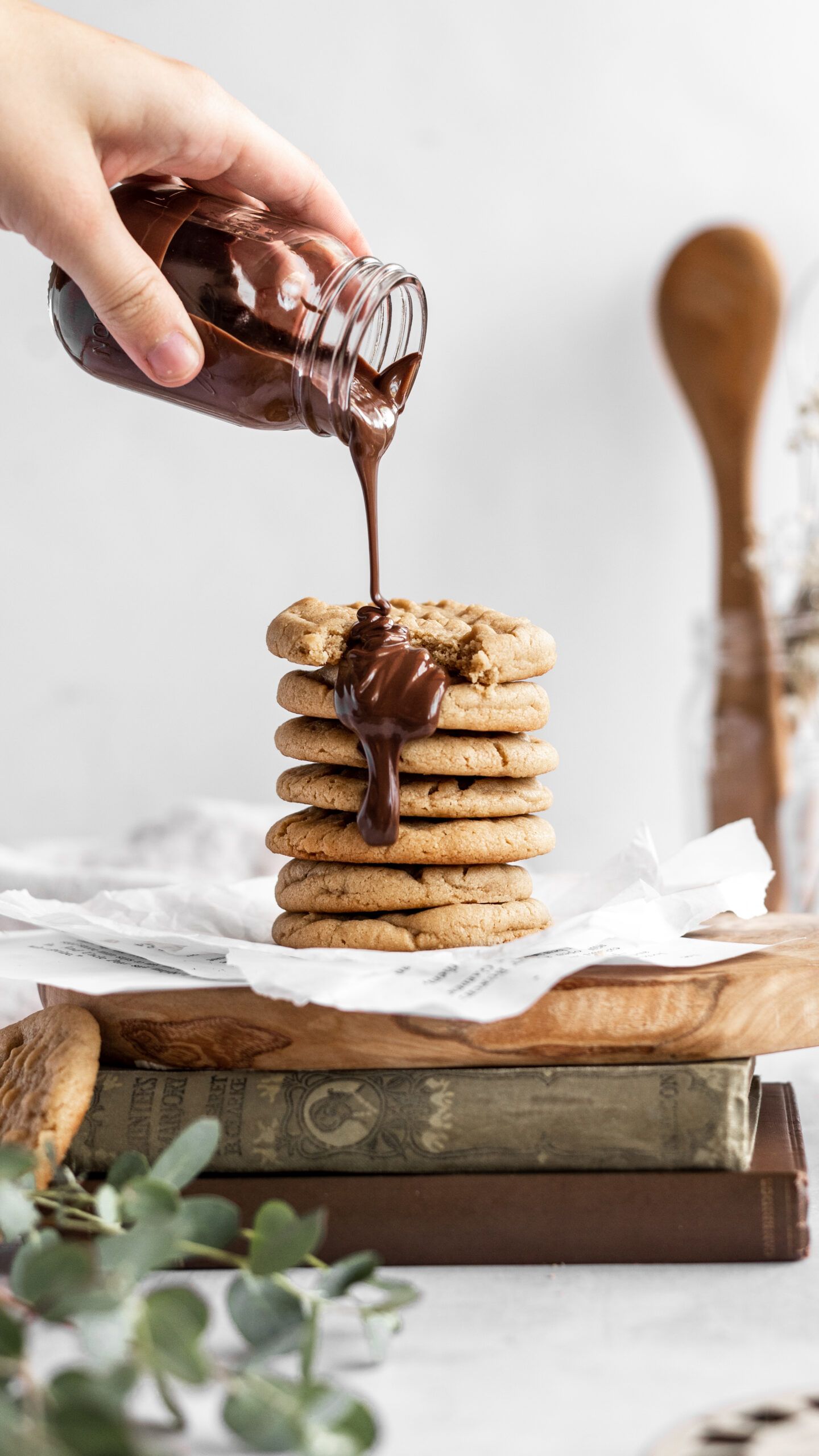 Rich chocolate sauce being poured over a stack of golden cookies on vintage books with rustic styling.
