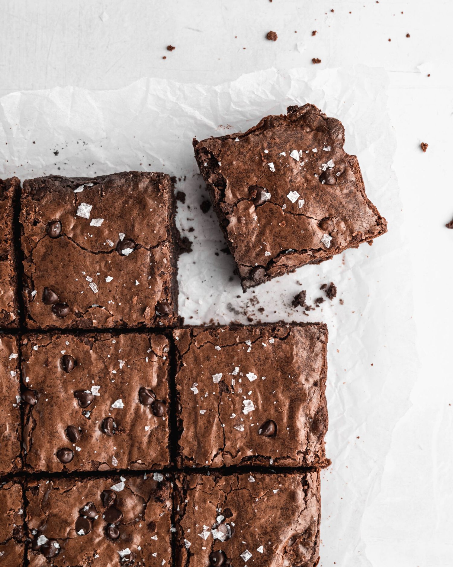 Freshly baked chocolate brownies topped with sea salt and cut into squares on parchment paper.