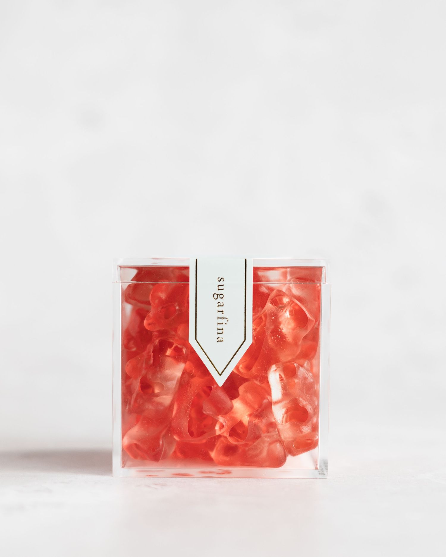 A clear square container filled with vibrant pink gummy bears against a white background.