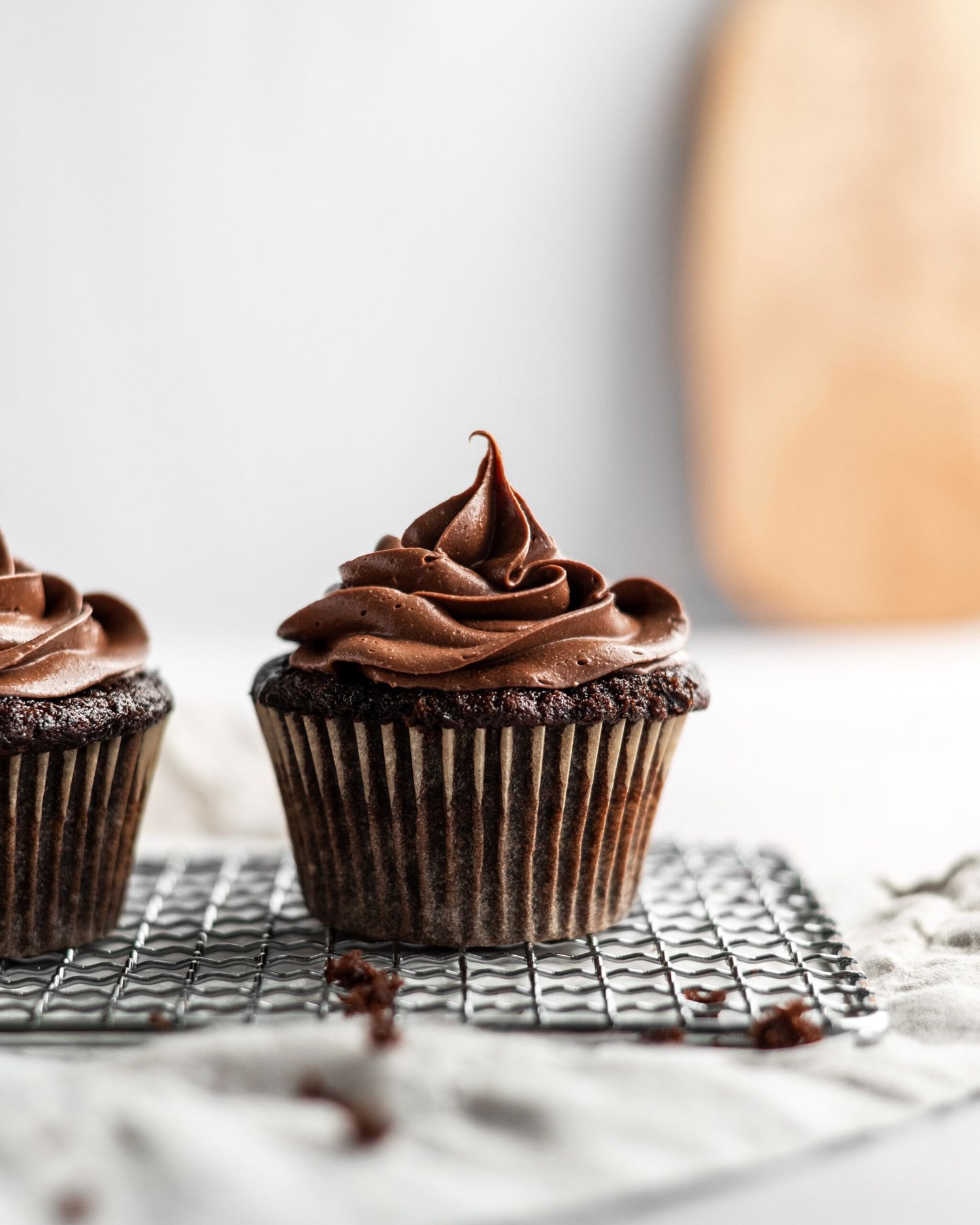 Chocolate cupcake with swirled chocolate frosting on a cooling rack against a light background.