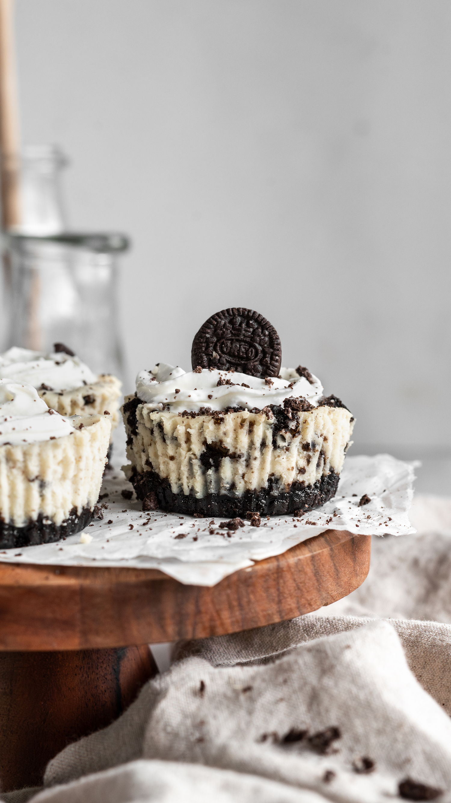 Mini cookies and cream cheesecakes topped with whipped cream and Oreo cookies on a wooden serving board.