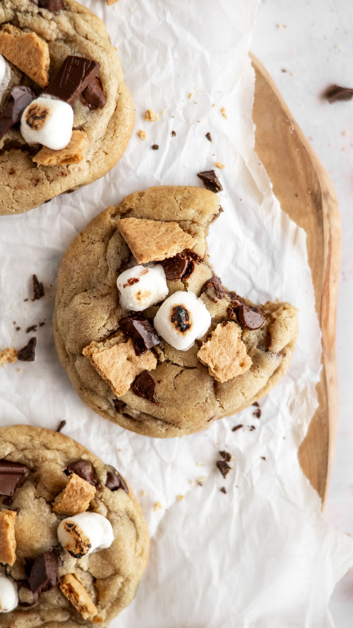 Homemade smores chocolate chip marshmallow cookies on parchment paper with scattered chocolate pieces.