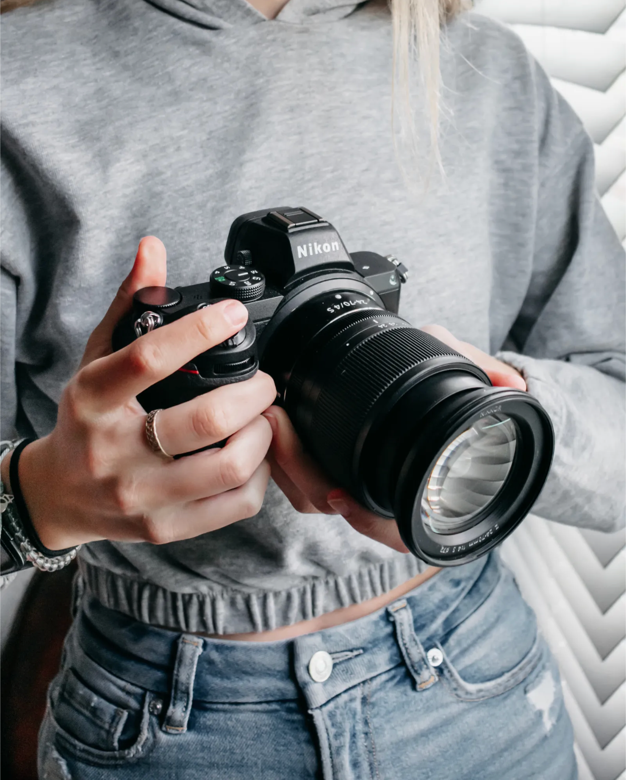 Camera lenses and equipment photographed against a gray sweatshirt and denim jeans background.