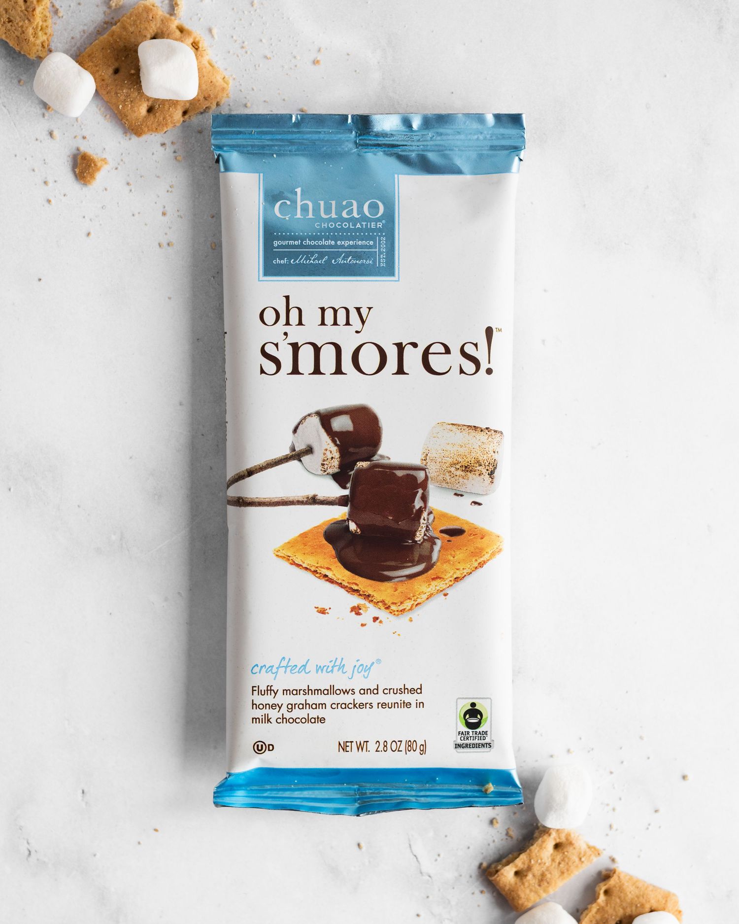 A package of Oh My S'mores chocolate treats with graham crackers scattered around on a light gray surface.