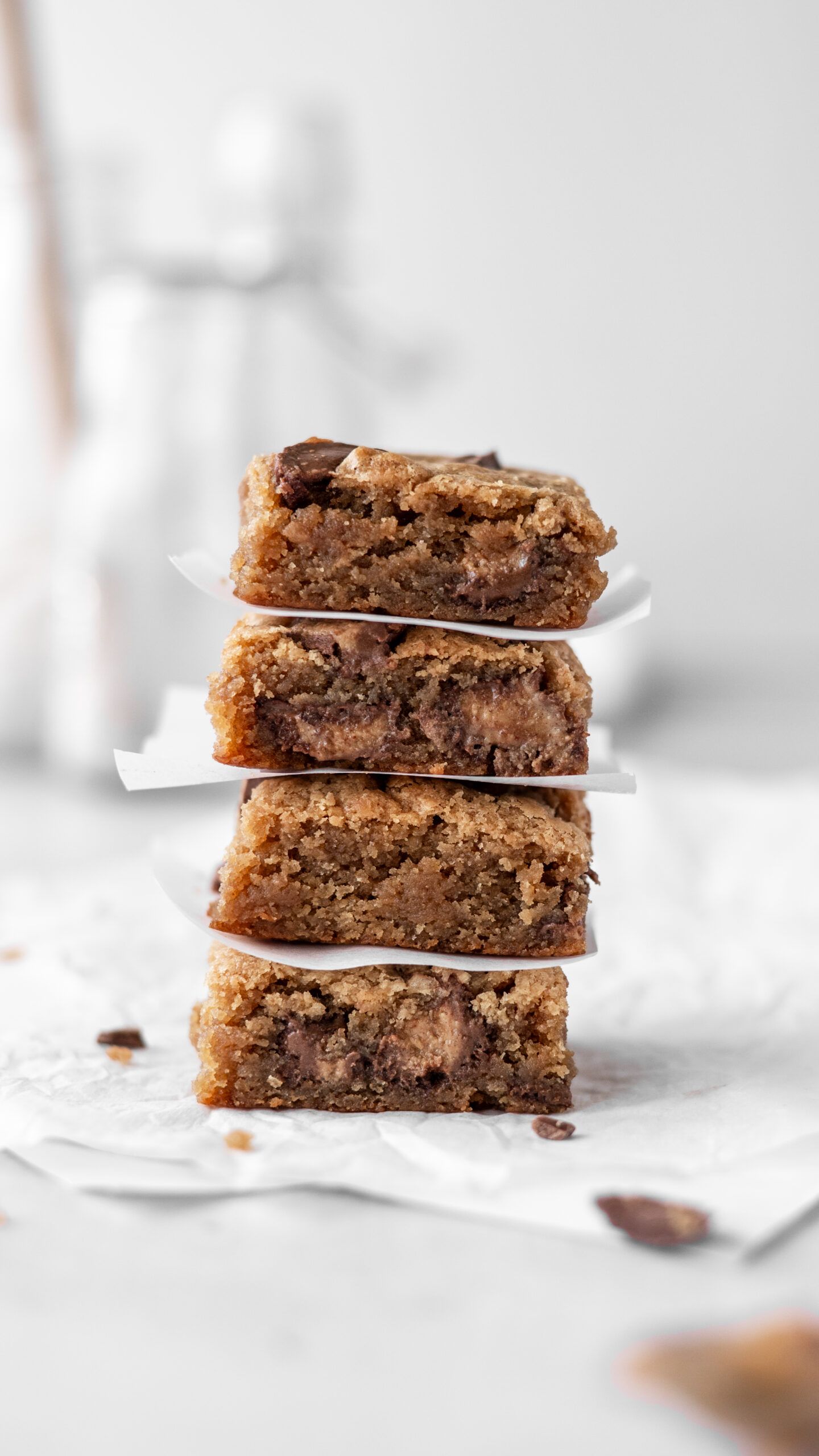 Stacked chocolate chip cookie bars with gooey centers on parchment paper against a light background.