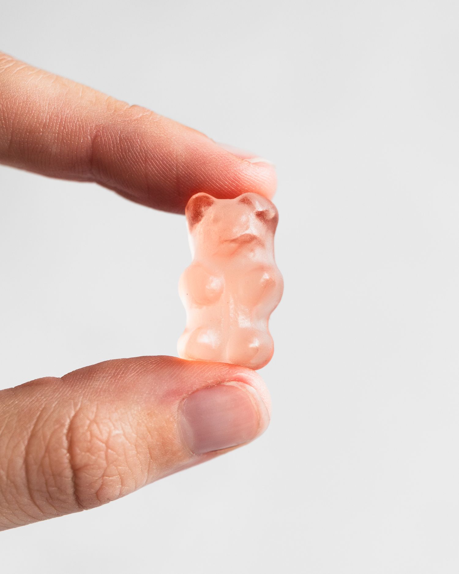 Close-up of fingers holding a translucent pink gummy bear candy against a white background.
