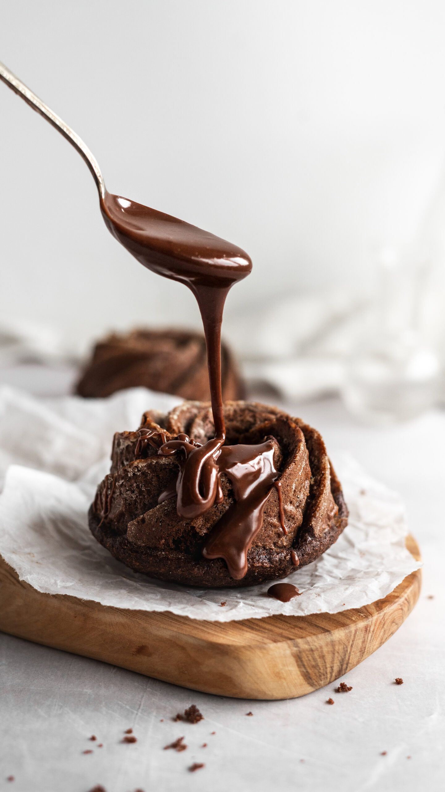 Hot ganache sauce being poured over a chocolate brownie on a wooden board.