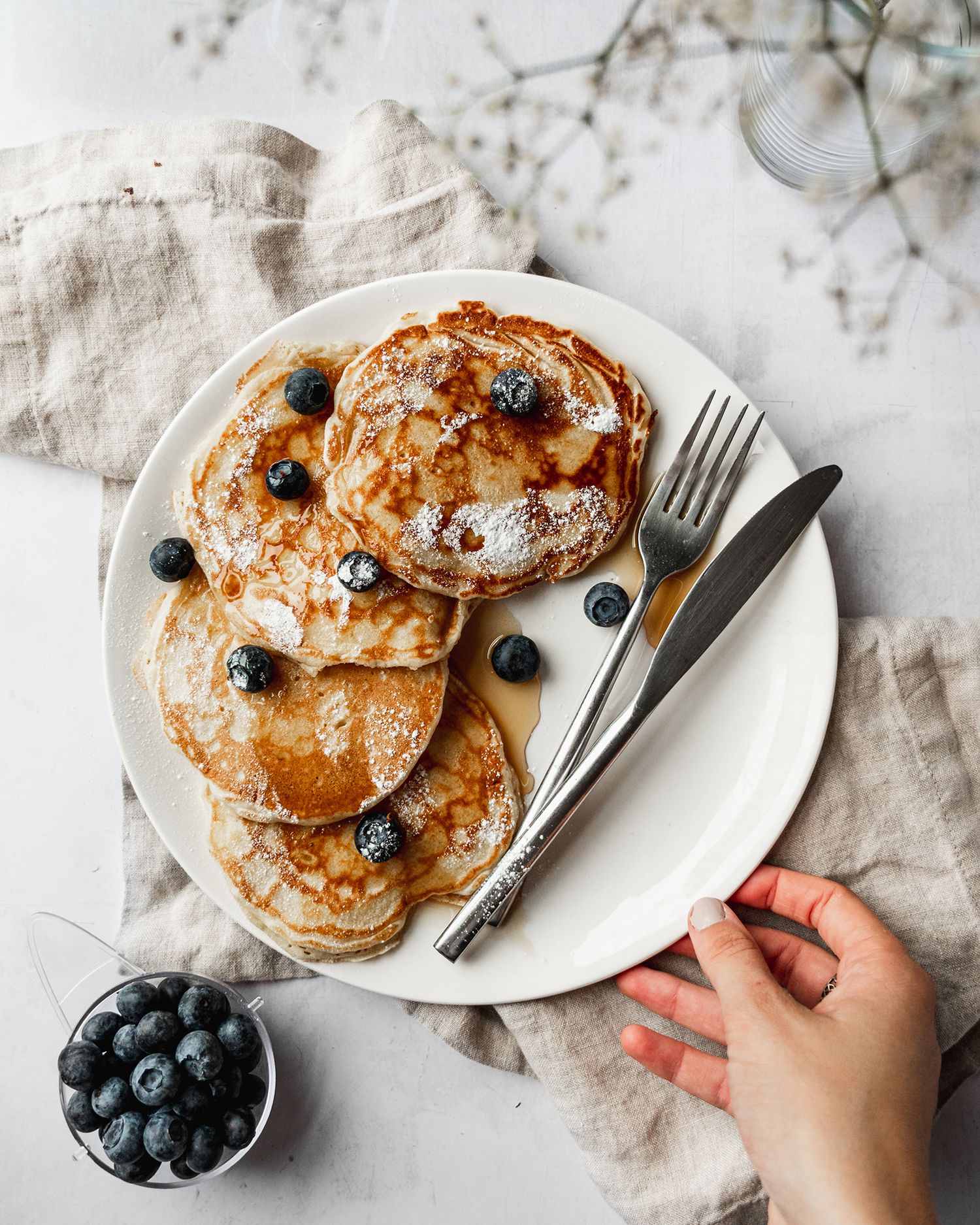 Golden pancakes topped with fresh blueberries and maple syrup on a white plate.
