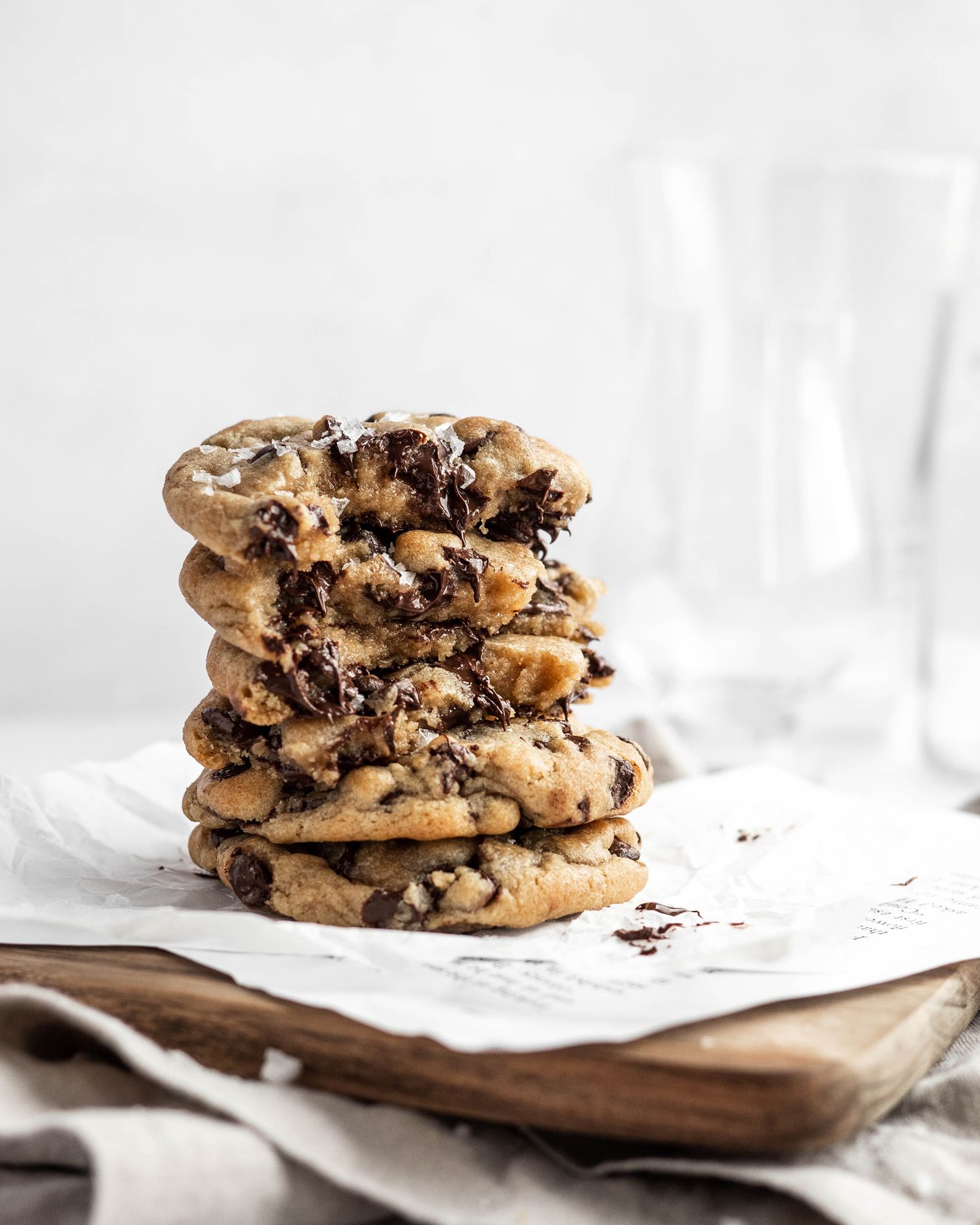 Stack of chocolate chip cookies on white parchment paper with crumbs scattered around.