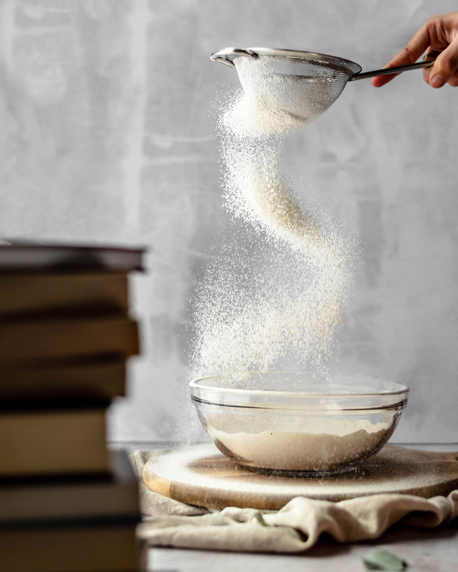 White sugar being poured from a measuring spoon onto a bowl on a rustic wooden table.