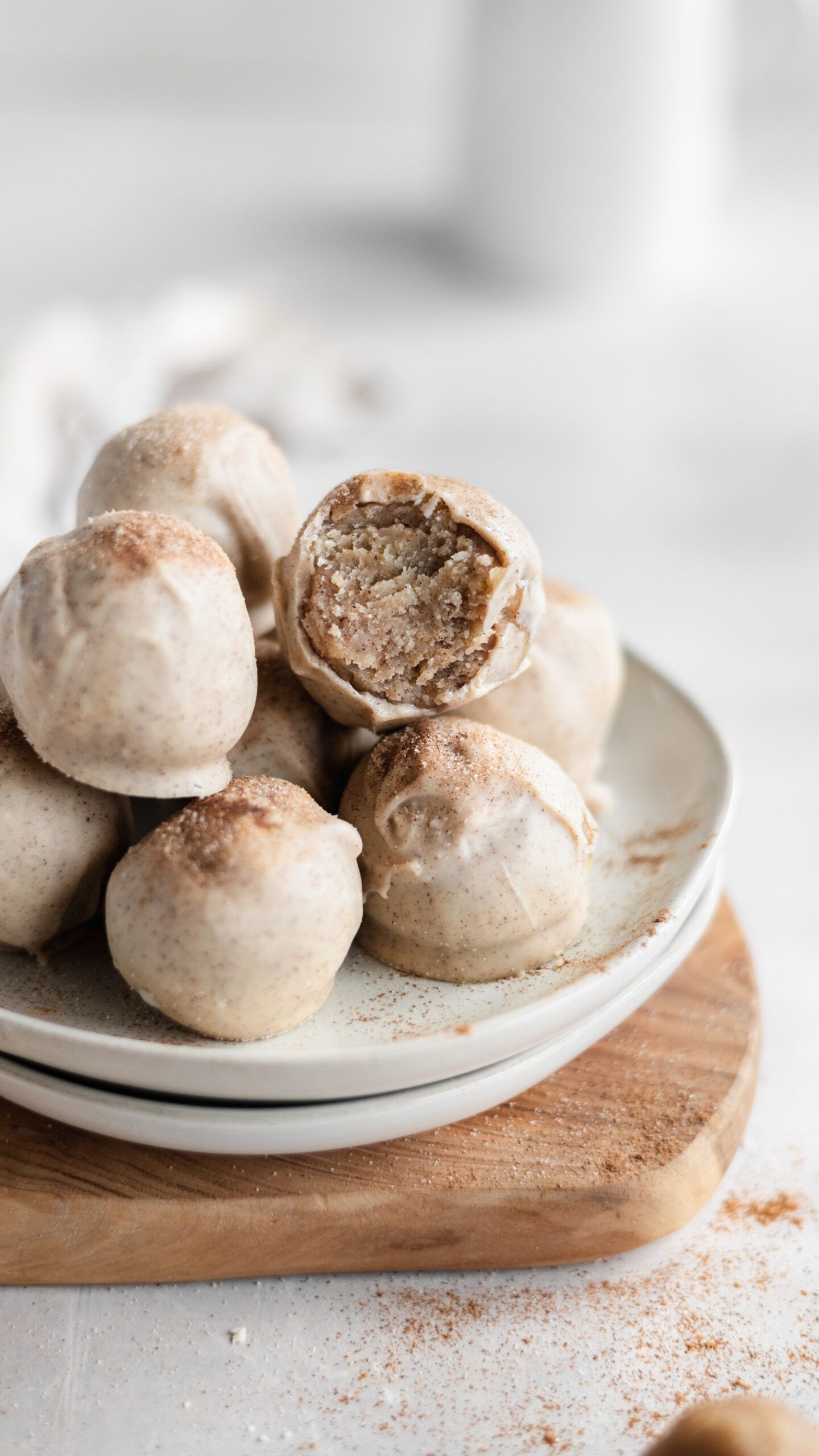 White chocolate truffles dusted with cocoa powder stacked on ceramic plates with one bitten to show creamy filling inside.