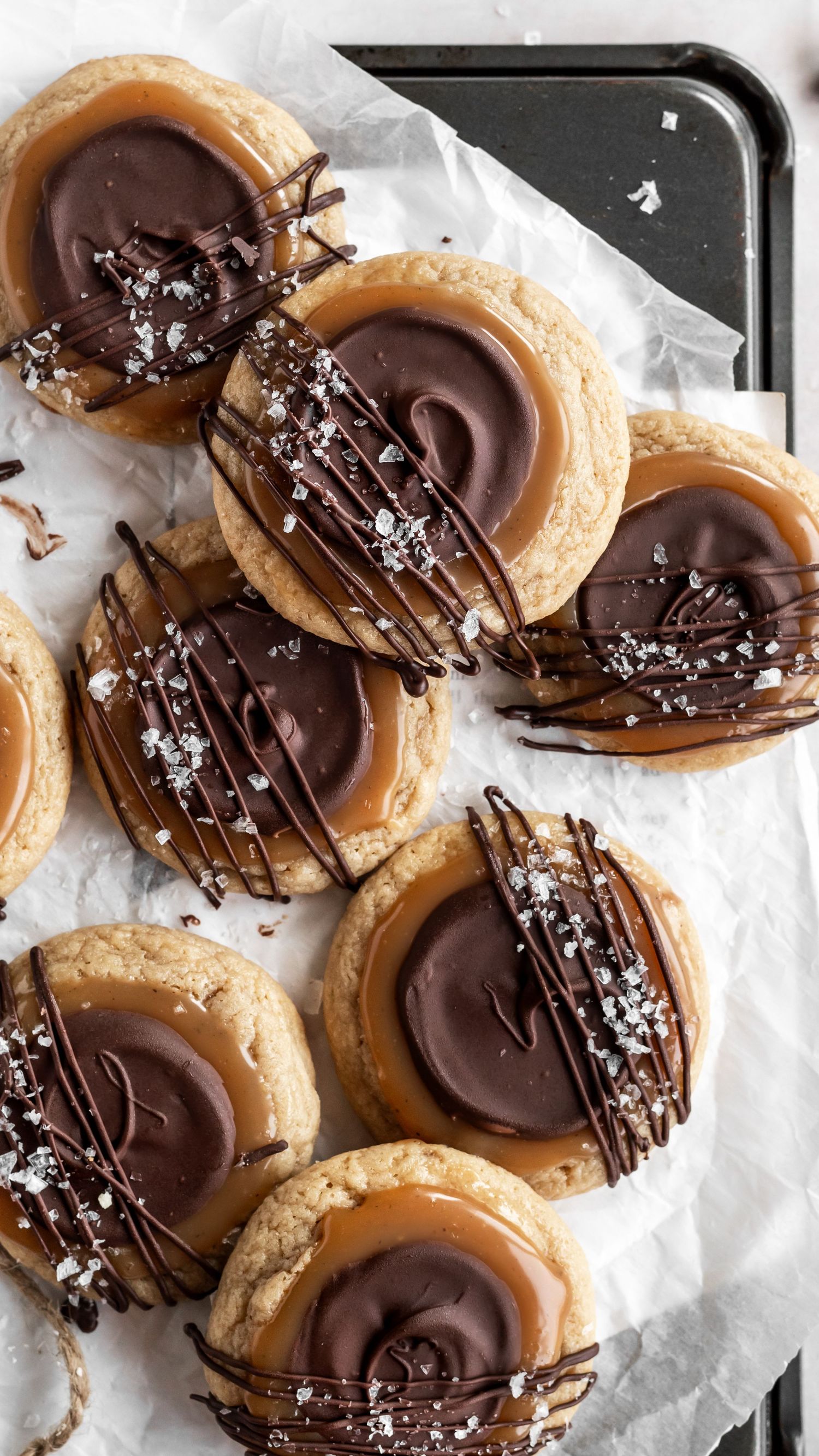 Chocolate dipped shortbread cookies with caramel and sea salt arranged on white parchment paper.