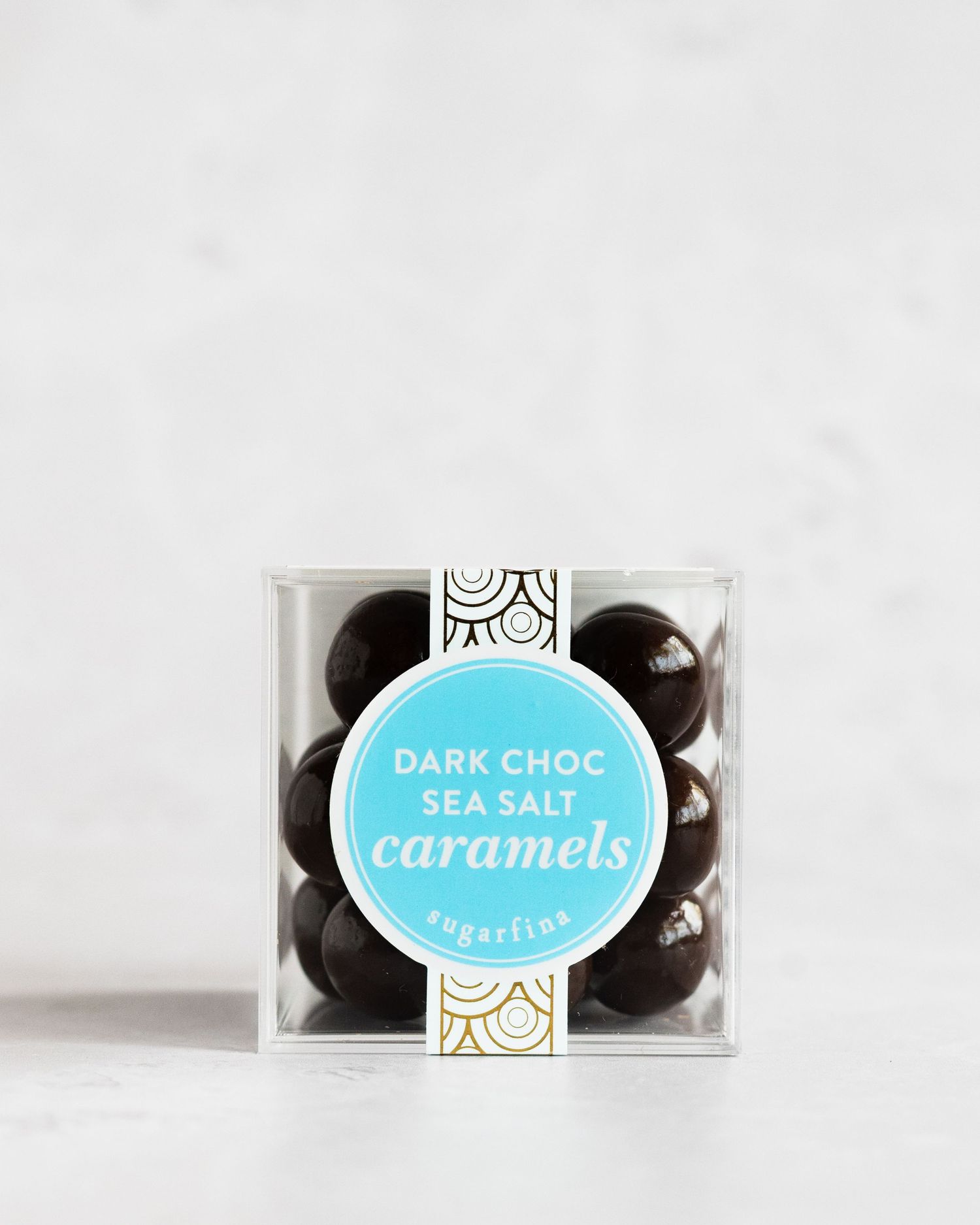 A clear box of dark chocolate sea salt caramels against a white background.