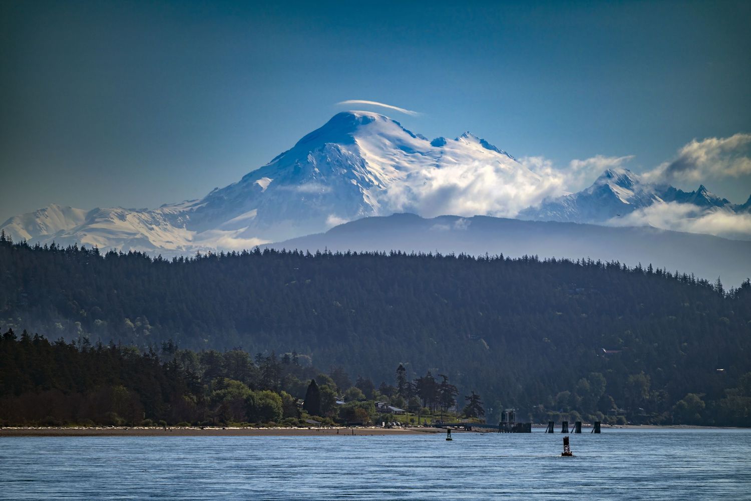 Snow-capped Mount Baker rising above forested shoreline and calm waters, captured from San Juan Island on a clear Pacific Northwest day