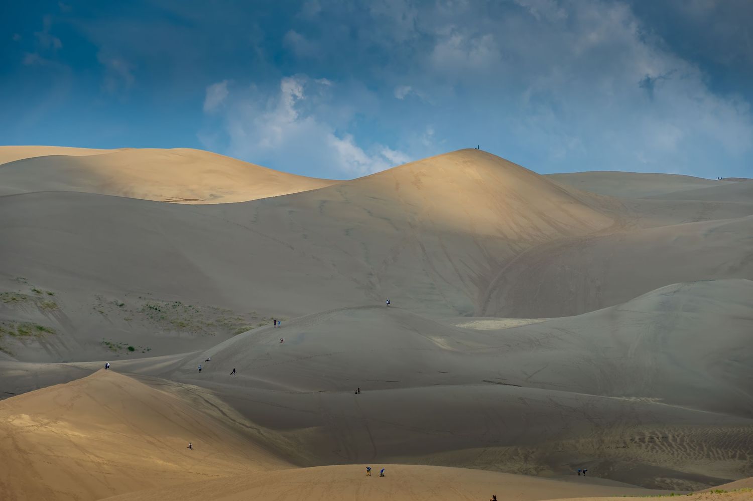 Golden sand dunes rising beneath dramatic clouds at Great Sand Dunes National Park in Colorado, with hikers exploring the vast landscape