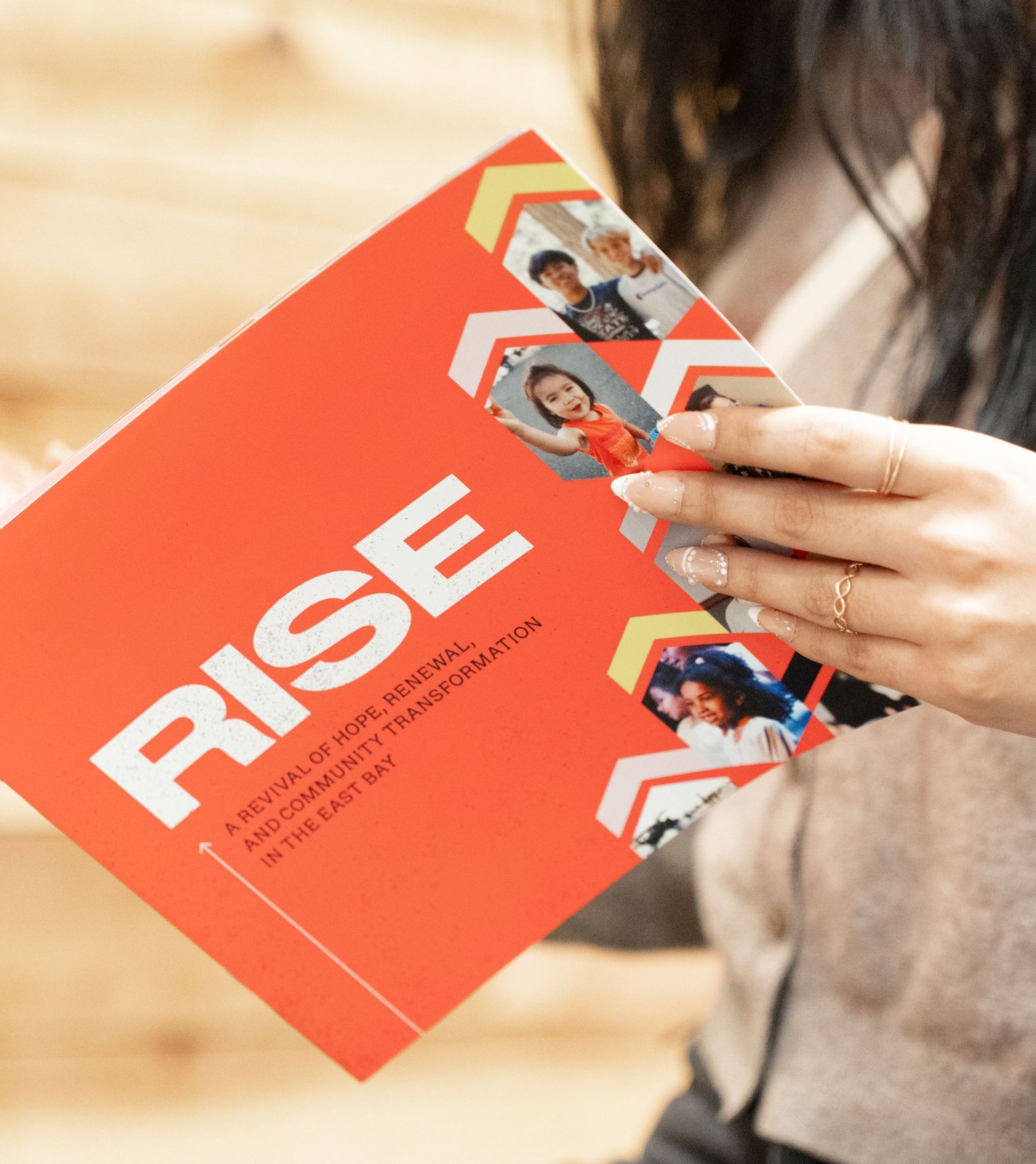 Someone holds a red RISE publication featuring profile photos and organizational content.