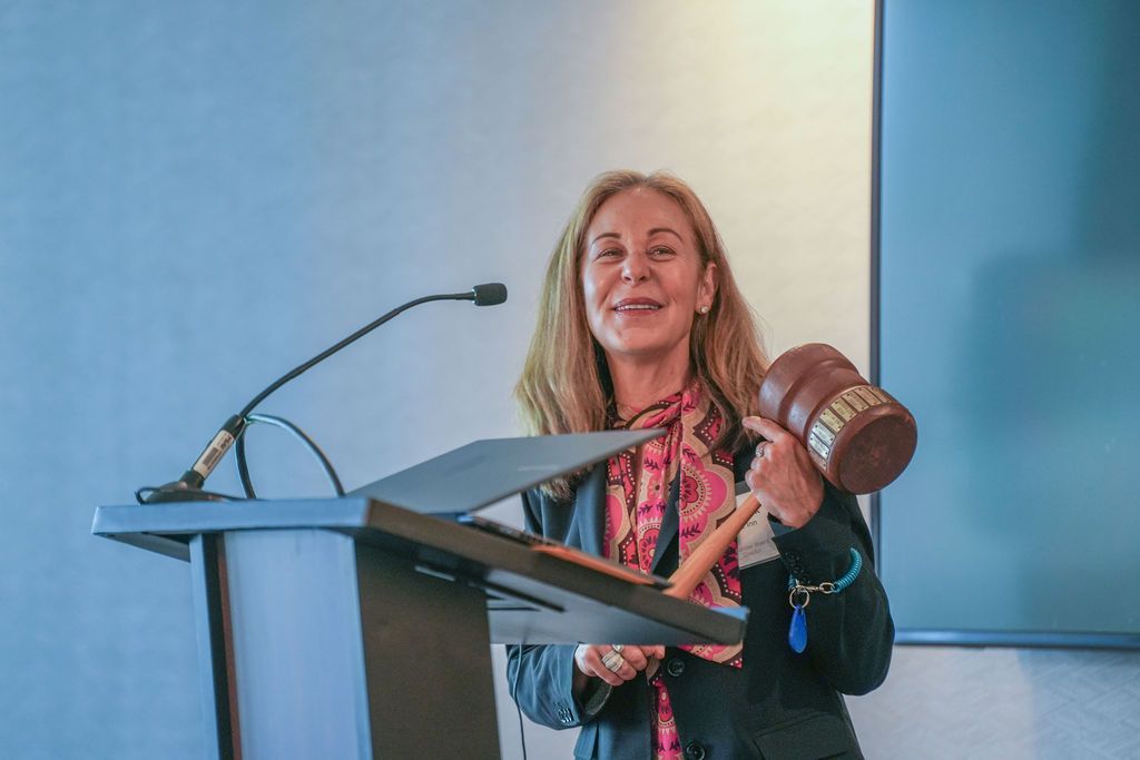 A speaker smiles while holding a ceremonial gavel at the podium during the Berkeley Chamber of Commerce annual meeting.