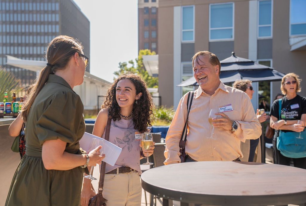 Guests chat and laugh around a high-top table on the Residence Inn Berkeley rooftop terrace during a Berkeley Chamber of Commerce networking