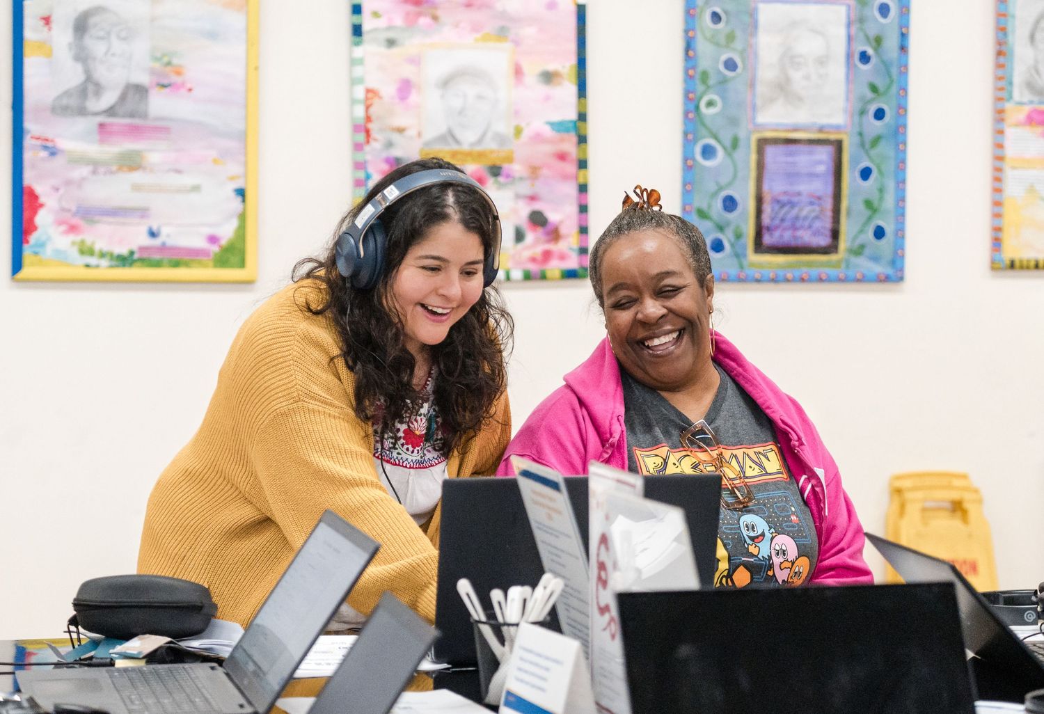 Two colleagues share a laugh while working together at a computer station.