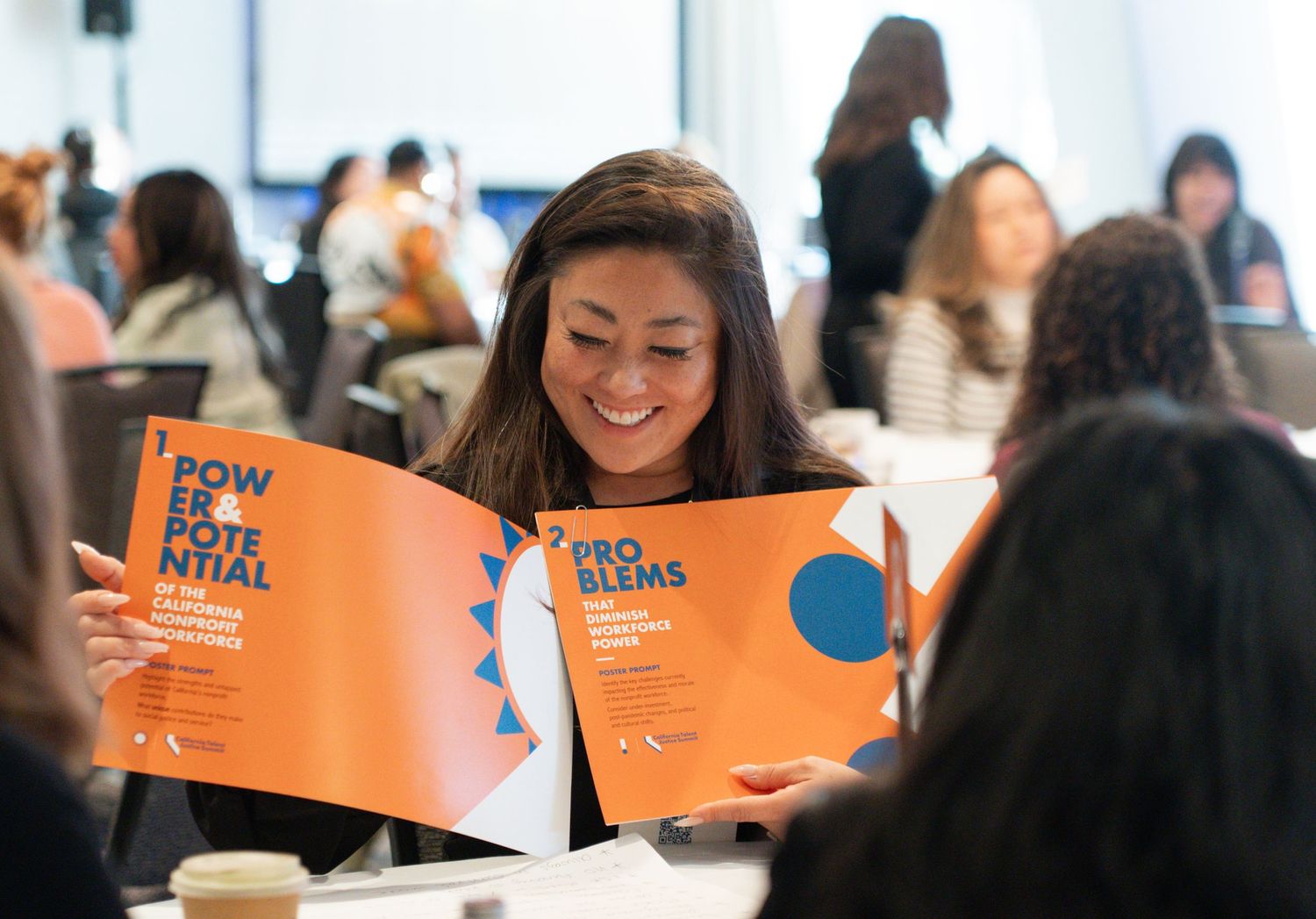 Group workshop scene with orange folders and participants seated at tables.