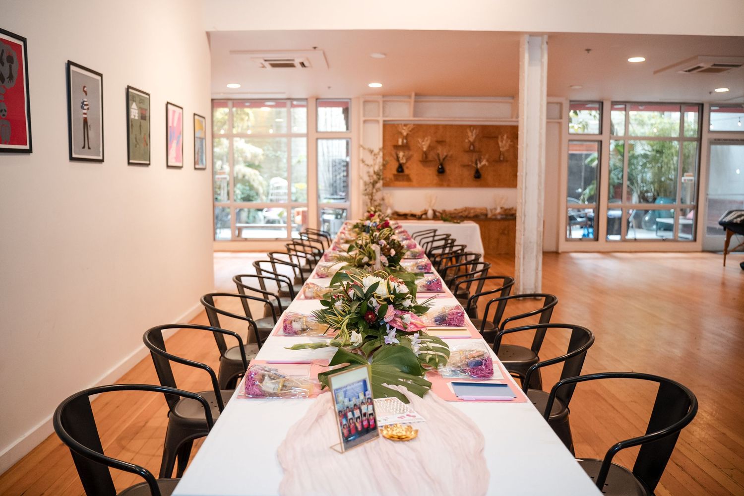 Modern dining room with long wooden tables, black chairs, and large windows overlooking a garden setting.