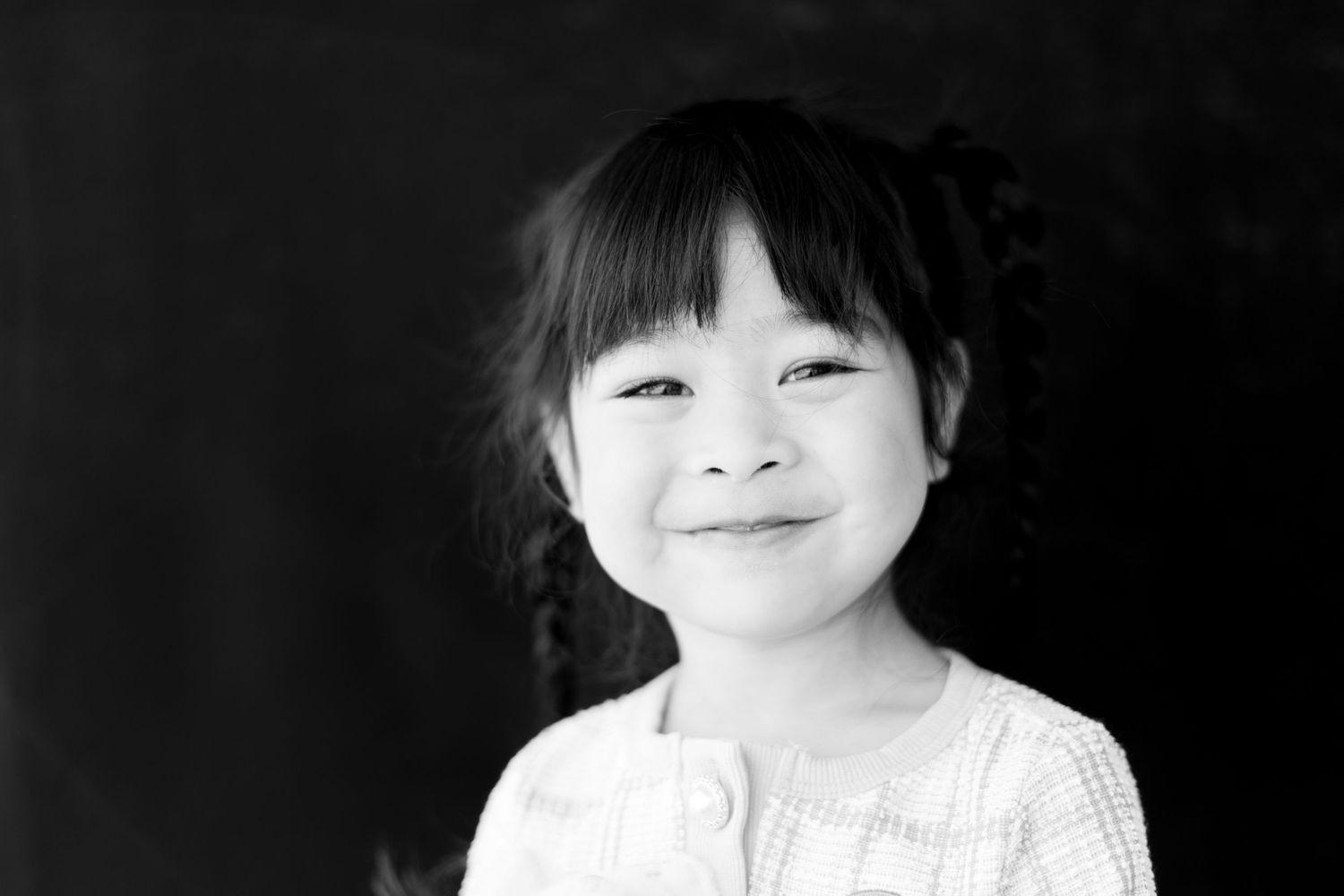 Black and white portrait of a young elementary school student smiling with bangs against a dark background.