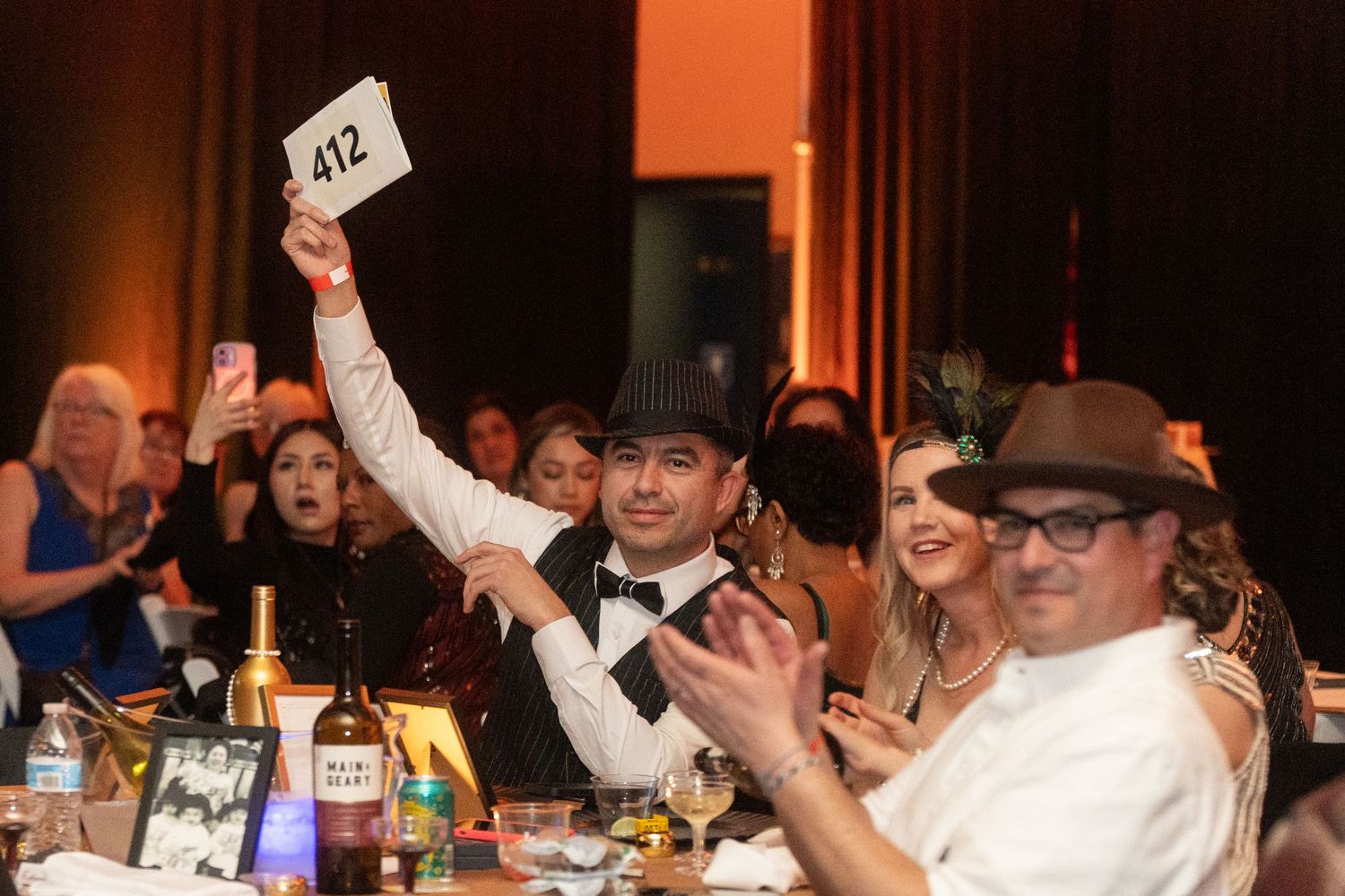 Attendees celebrate at a lively dinner event with table number cards and drinks.