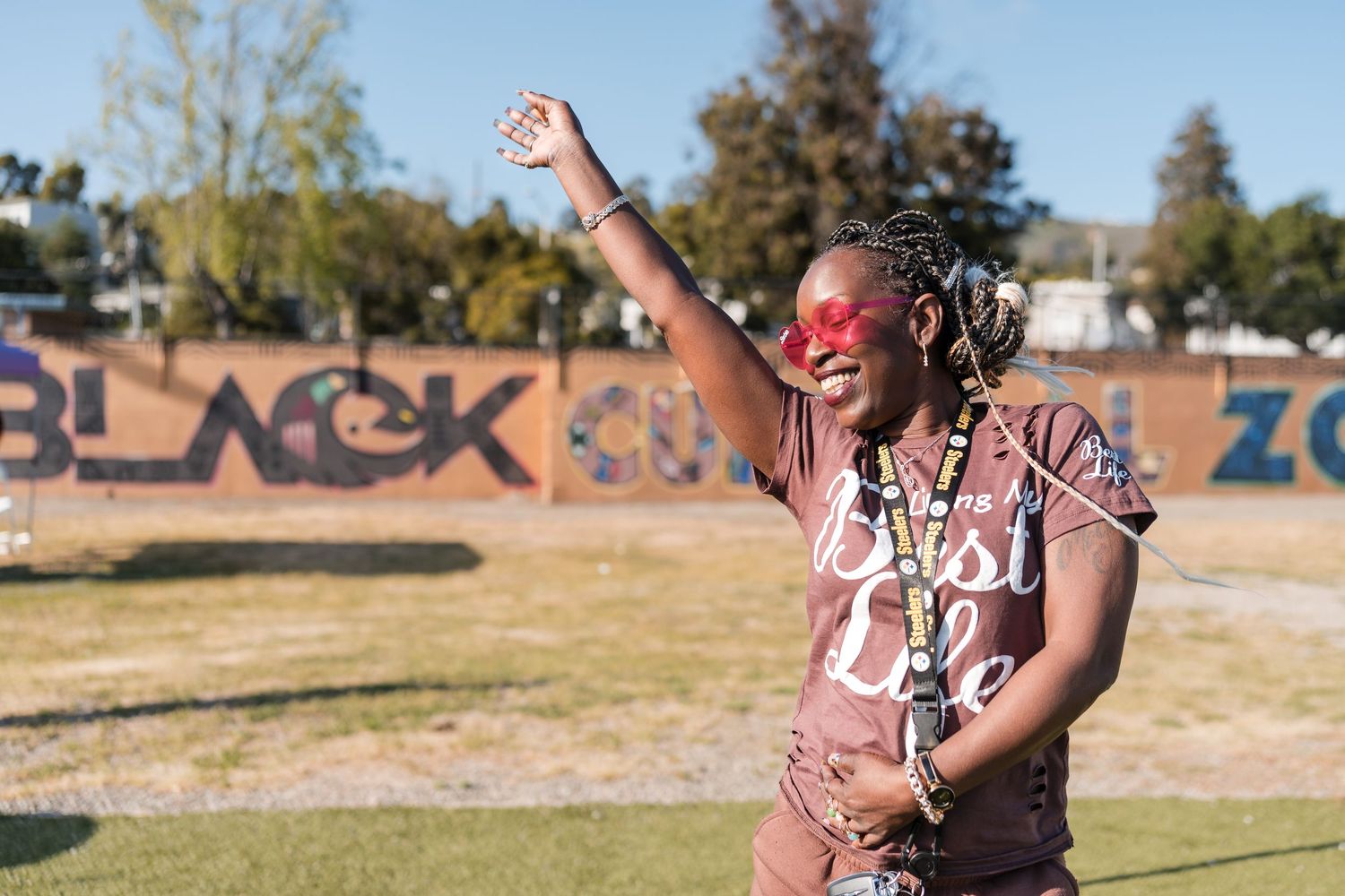 A person in red sunglasses celebrates joyfully in front of outdoor graffiti art.