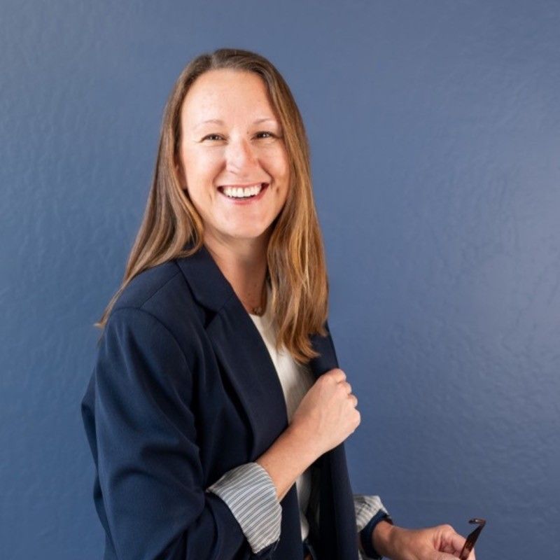 Professional woman in navy blazer smiling warmly against blue background.