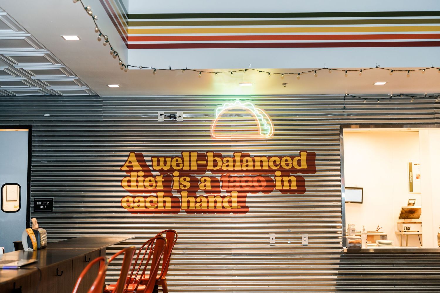 Illuminated orange neon sign reading 'Well balanced' mounted on a corrugated metal wall in a modern interior space.