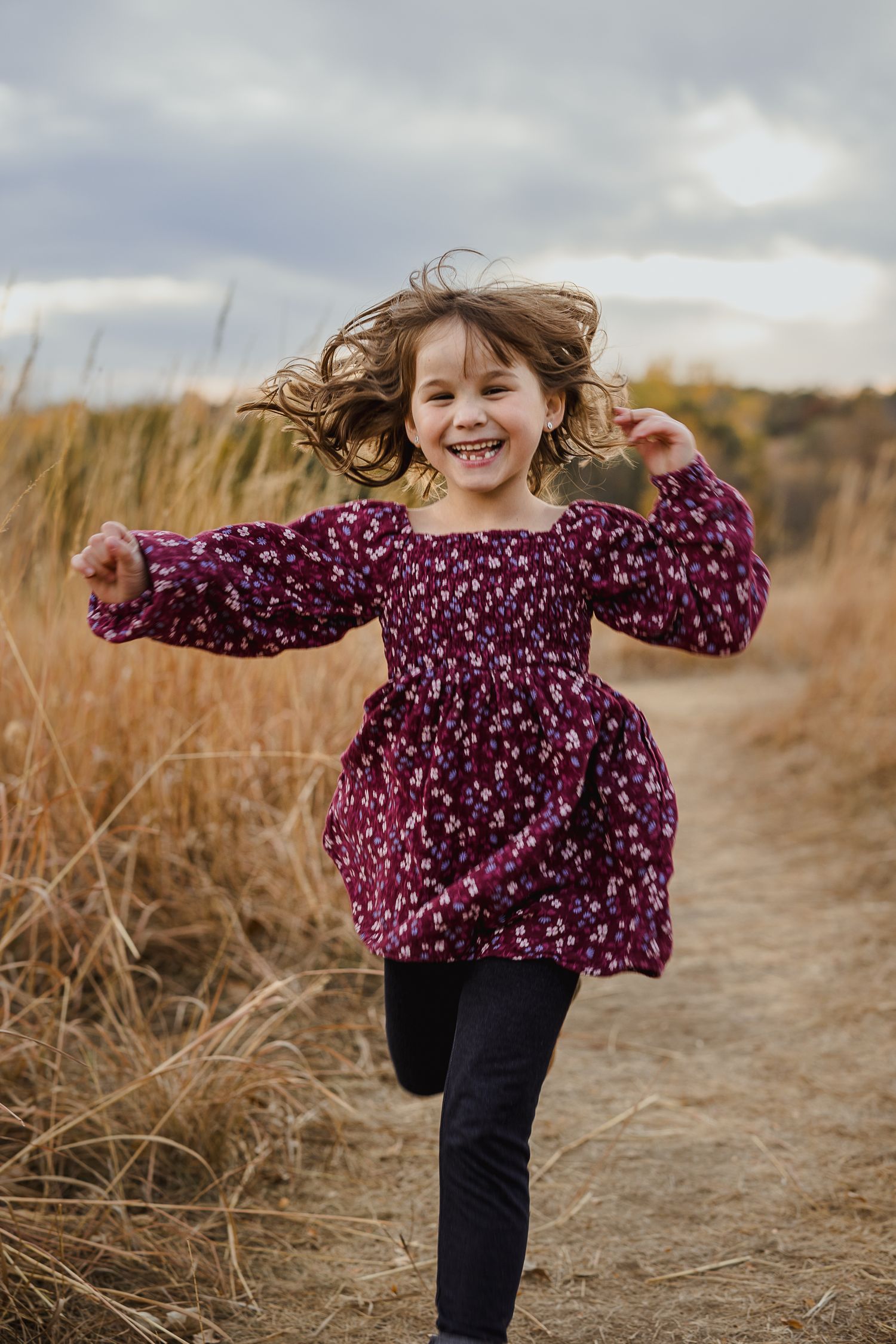 Young child in purple floral top running and playing in autumn field.