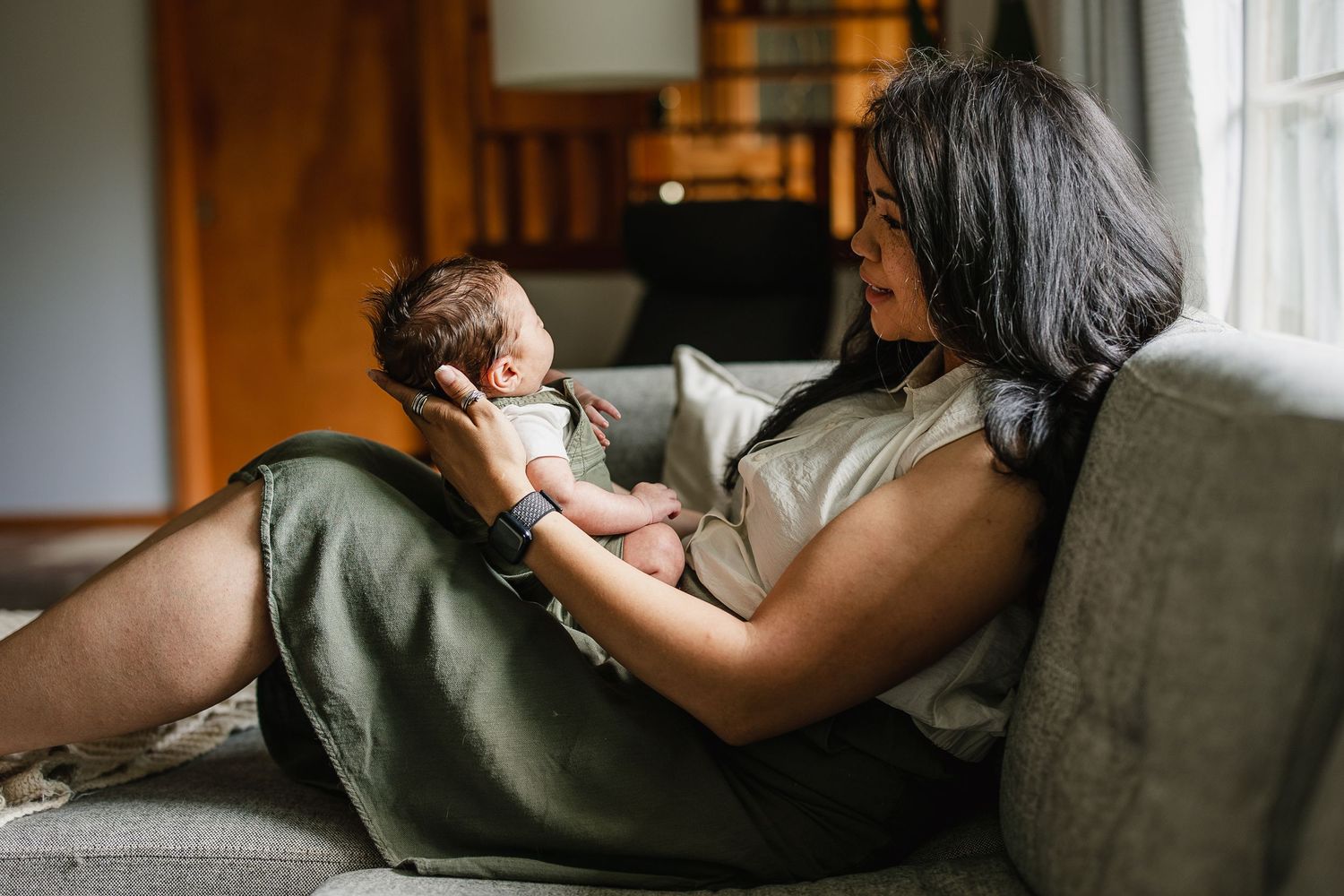 Mother cradling newborn baby on couch at home, sharing a tender bonding moment in a cozy living room.