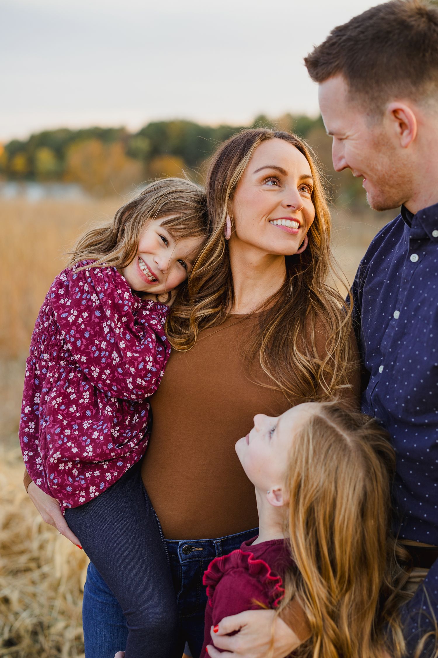Family wearing coordinated autumn outfits embracing in field at sunset.