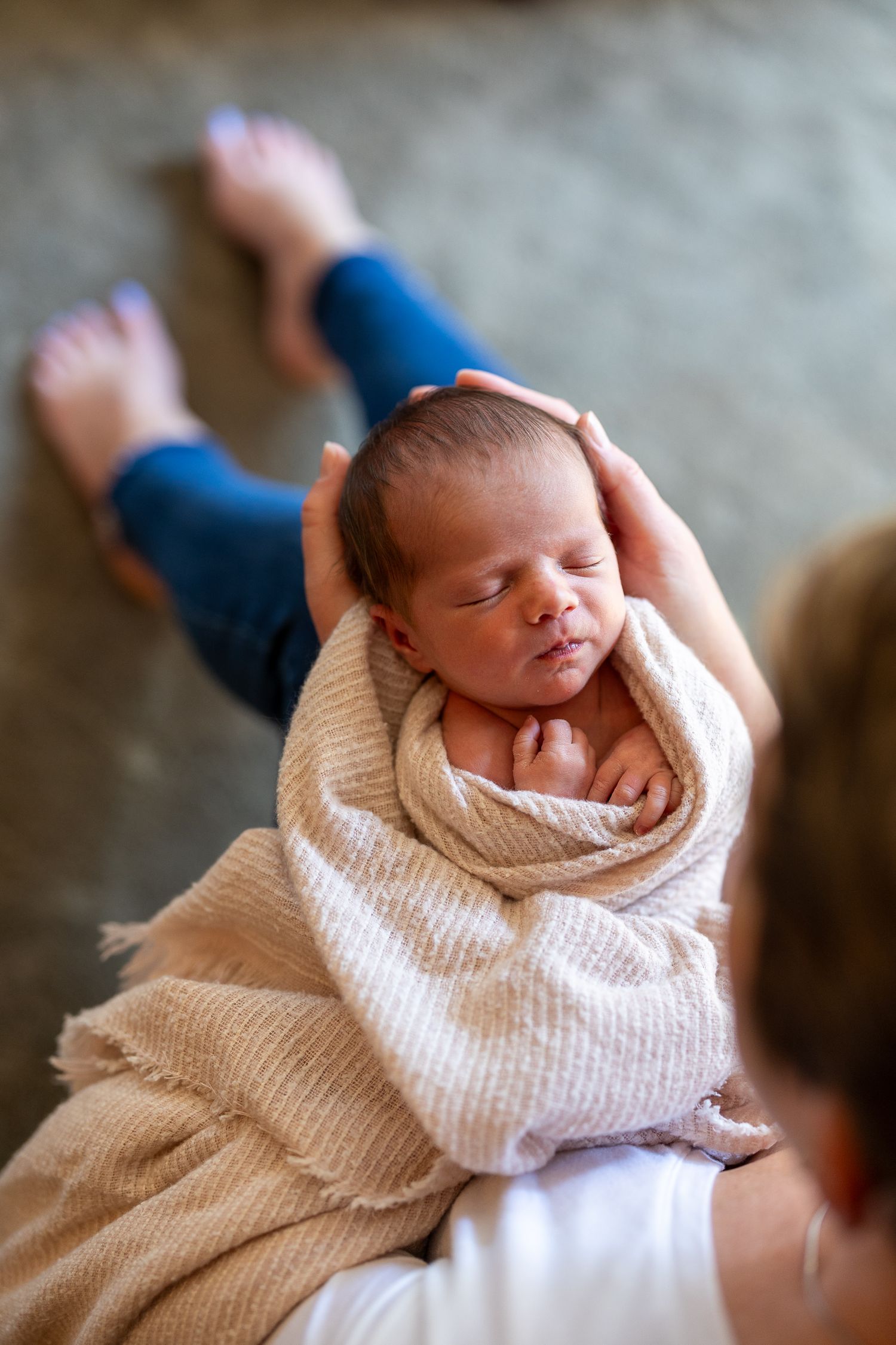 A newborn baby swaddled in a beige blanket sleeping peacefully in a mother's arms.